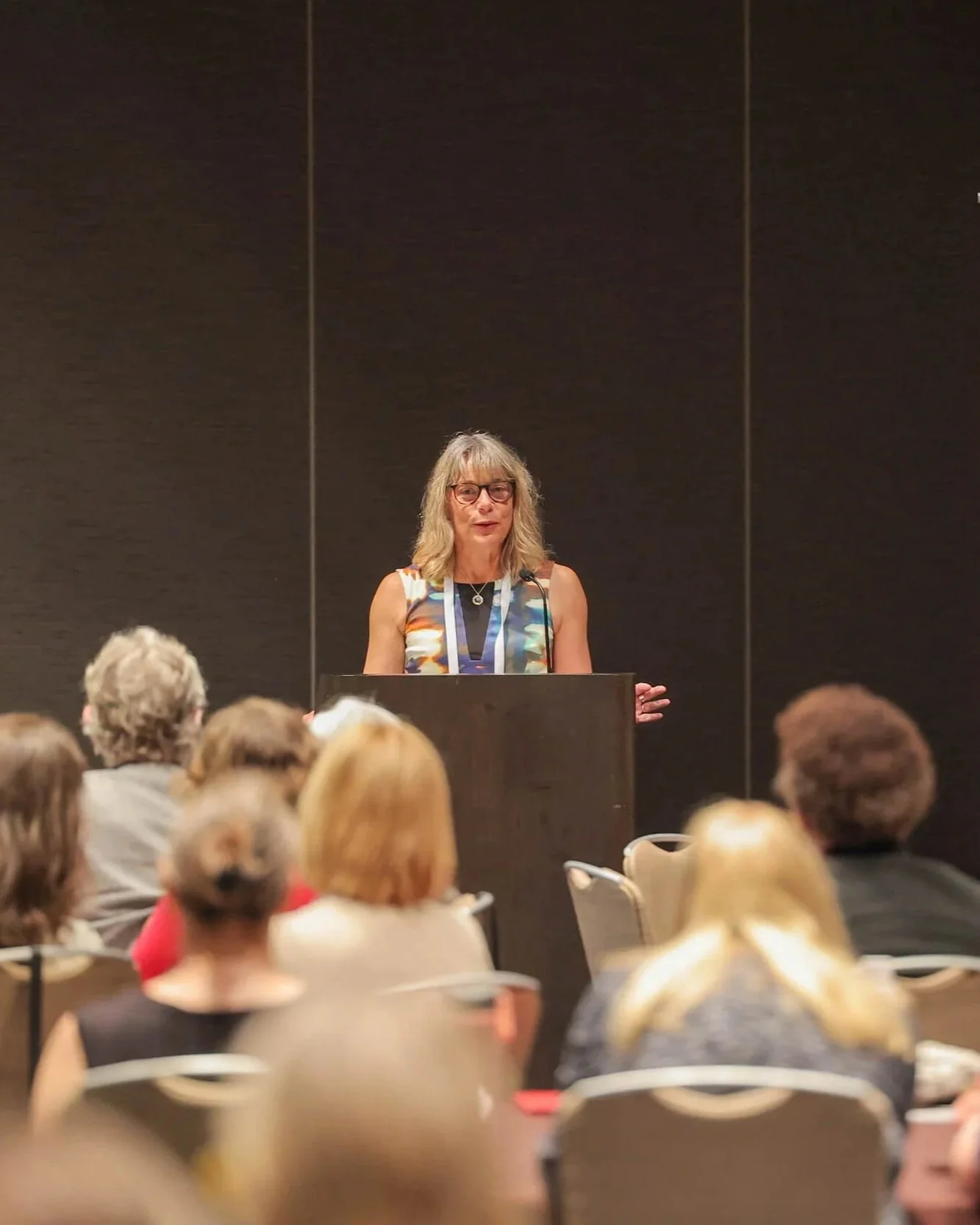 Dashka Slater speaking at a podium to an audience during a conference session.
