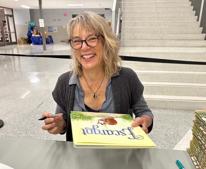 Dashka Slater smiling while signing a copy of her picture book “Escargot” at a book event.
