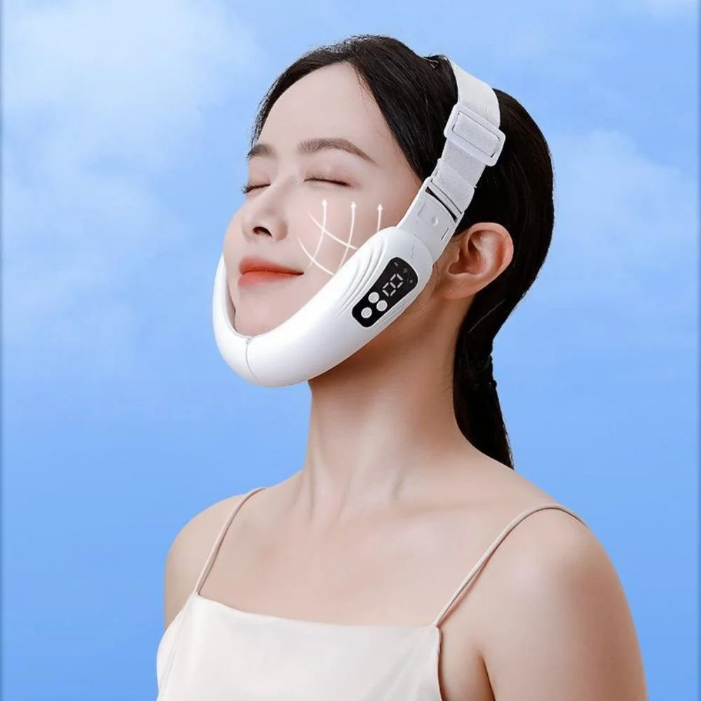 Woman with eyes closed wearing a white facial massage or skincare device with digital controls against a blue sky background.