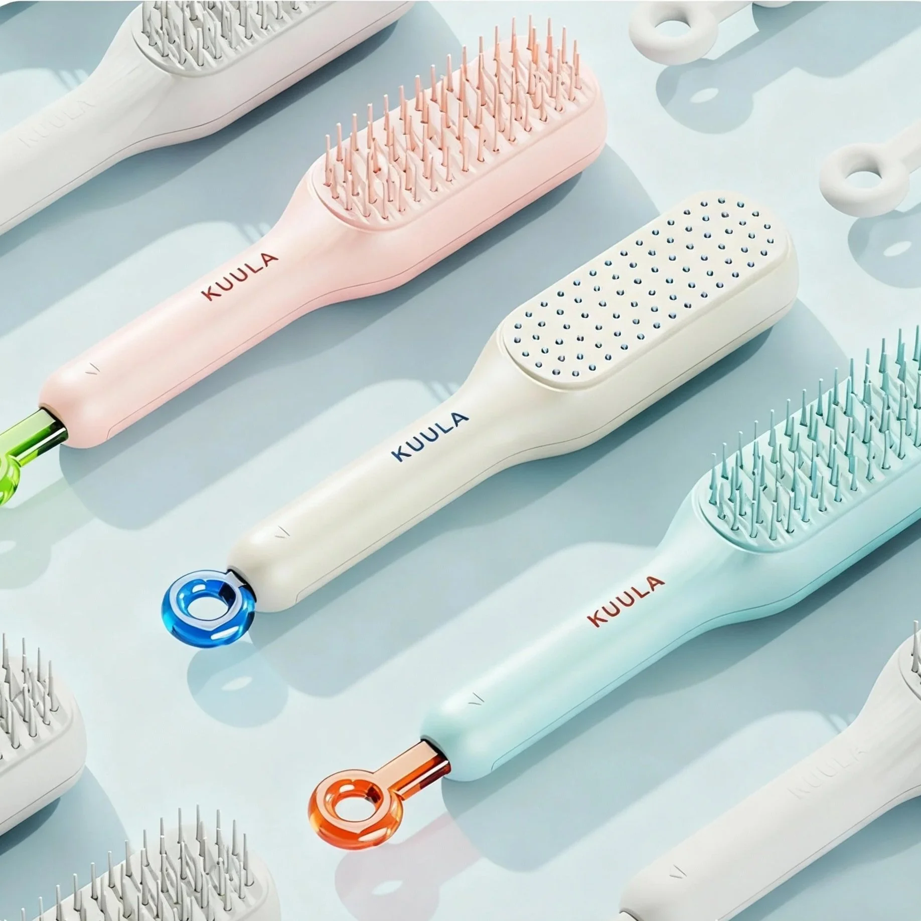 Colorful hairbrushes with rounded handles in pink, white, and blue, placed on a light blue surface.