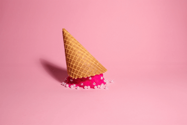 Eistüte auf pinkem Hintergrund, das Eis steht auf einer rosa Substanz mit Perlen.