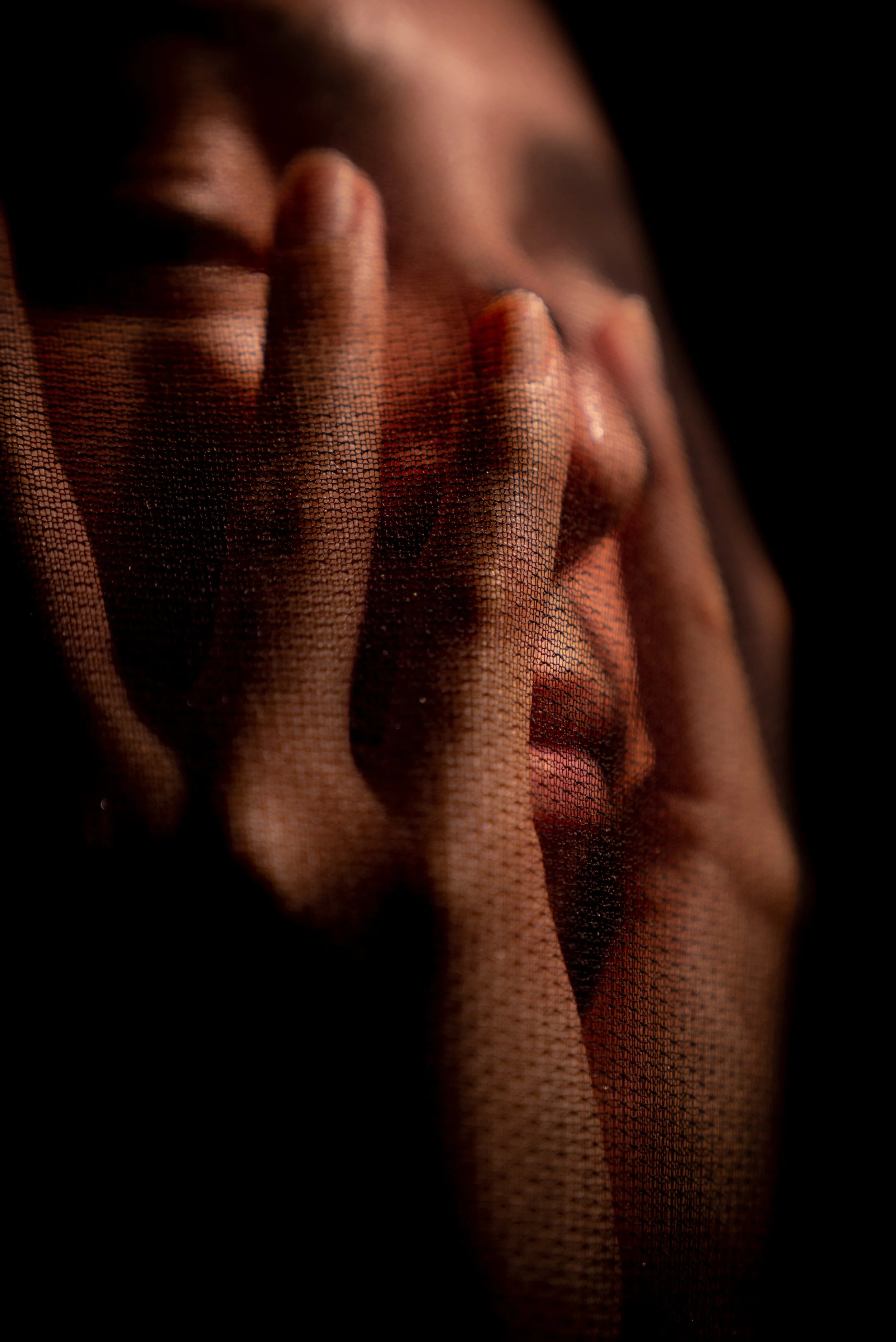 Nahaufnahme eines menschlichen Gesichts, das hinter einem dünnen, durchsichtigen Stoff verborgen ist, während eine Hand eine Geste auf das Gesicht legt.