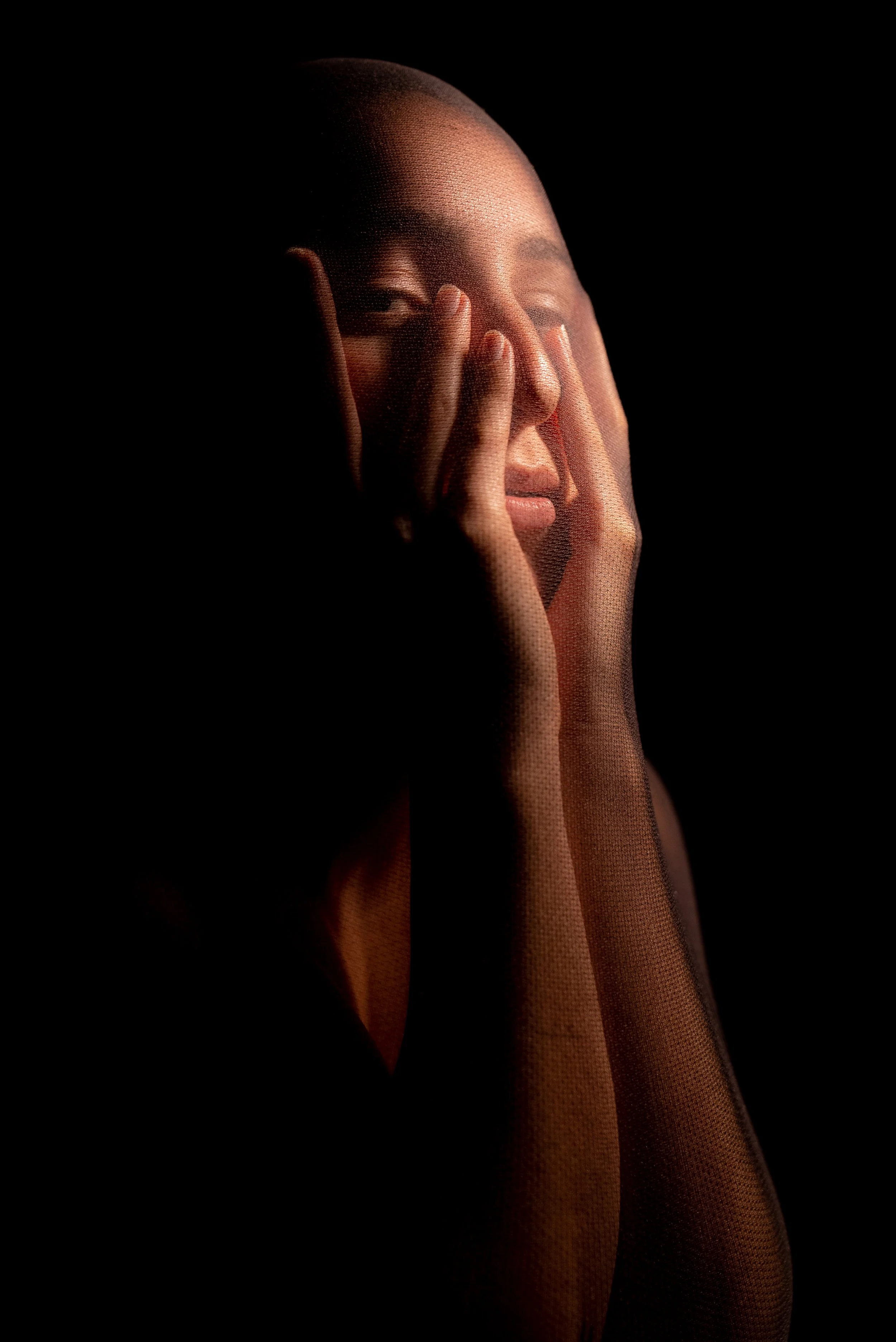 Nahaufnahme eines Mannes, der mit geschlossenen Augen gegen eine dunkle Oberfläche anlehnt, Hände auf Gesicht, sanftes Licht auf Gesicht und Hände, dramatischer Schatten.