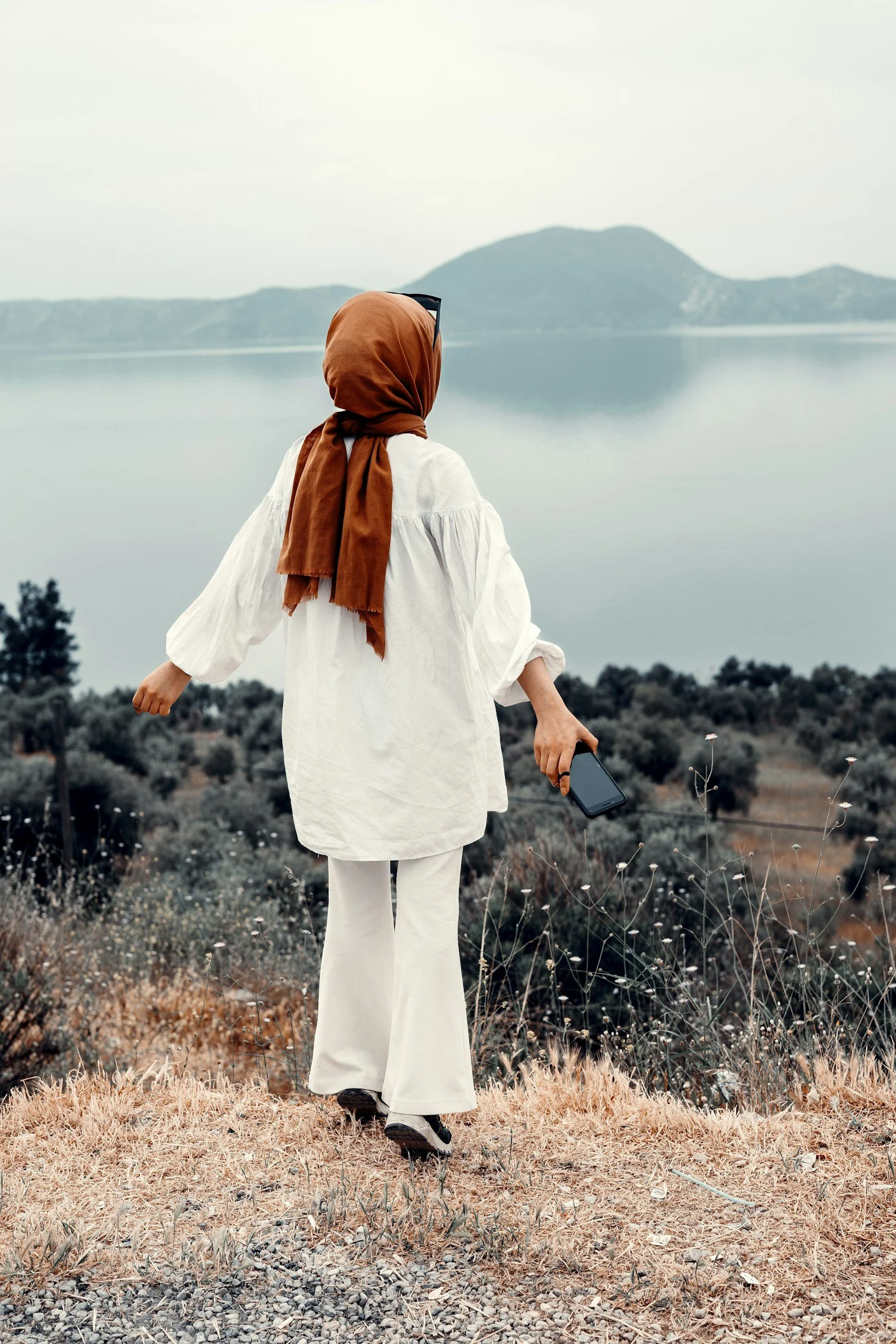 A smiling woman with shoulder-length black hair wearing a blue top in a lush greenhouse with green plants.