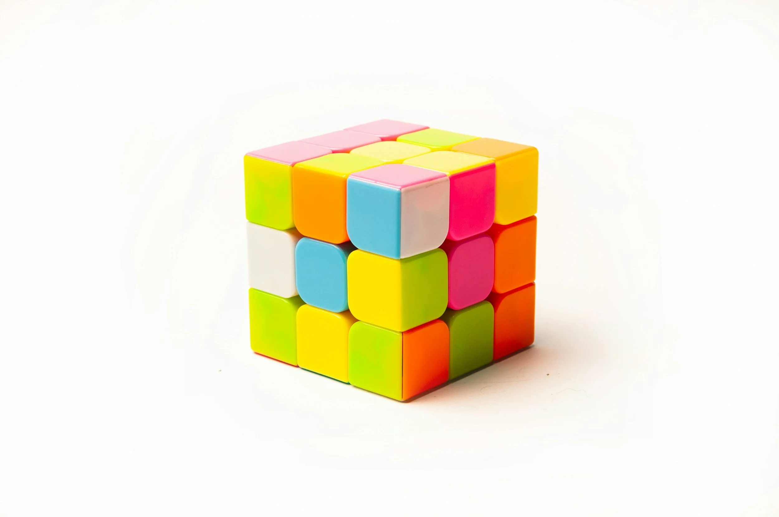 Colorful Rubik's Cube with pastel pink, blue, yellow, orange, and green stickers, reflected on a white surface.