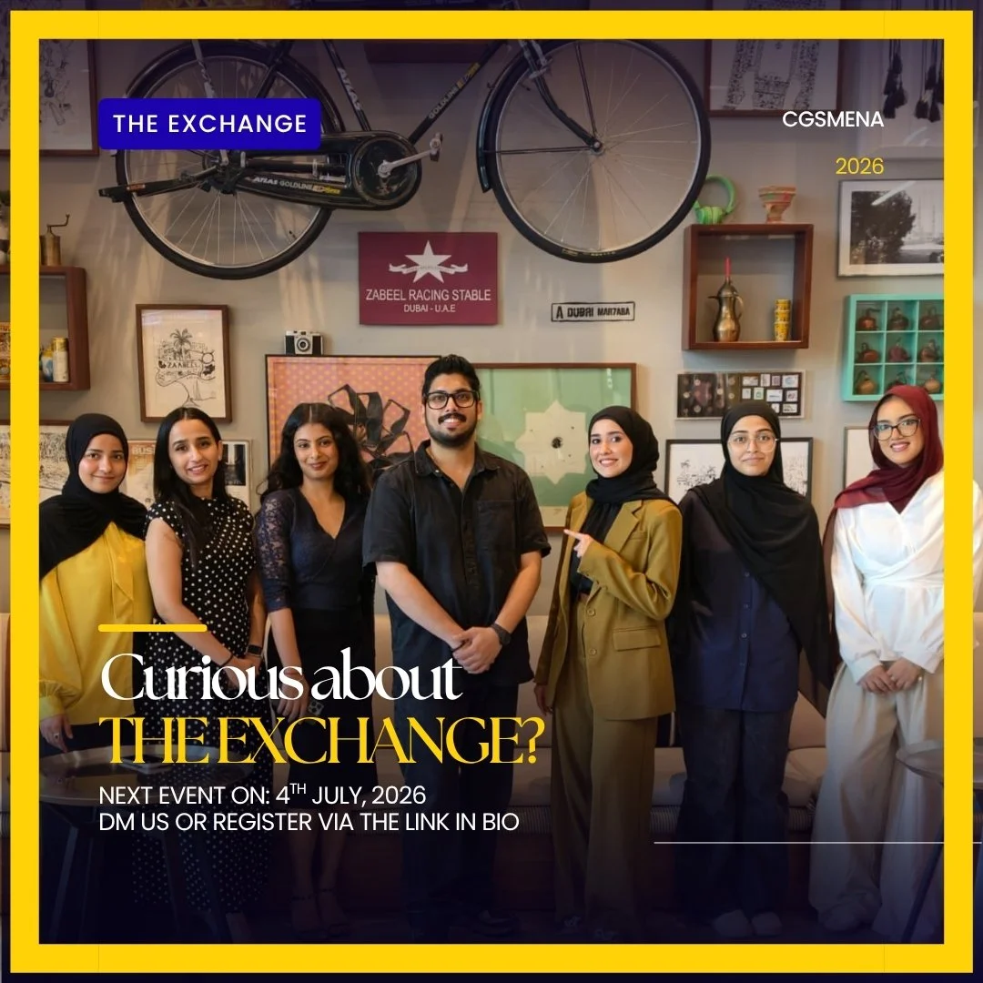A group of seven diverse women and one man standing together indoors, smiling for a photo. The background features various framed pictures, a bicycle mounted on the wall, and decorative items in a cozy, modern setting.