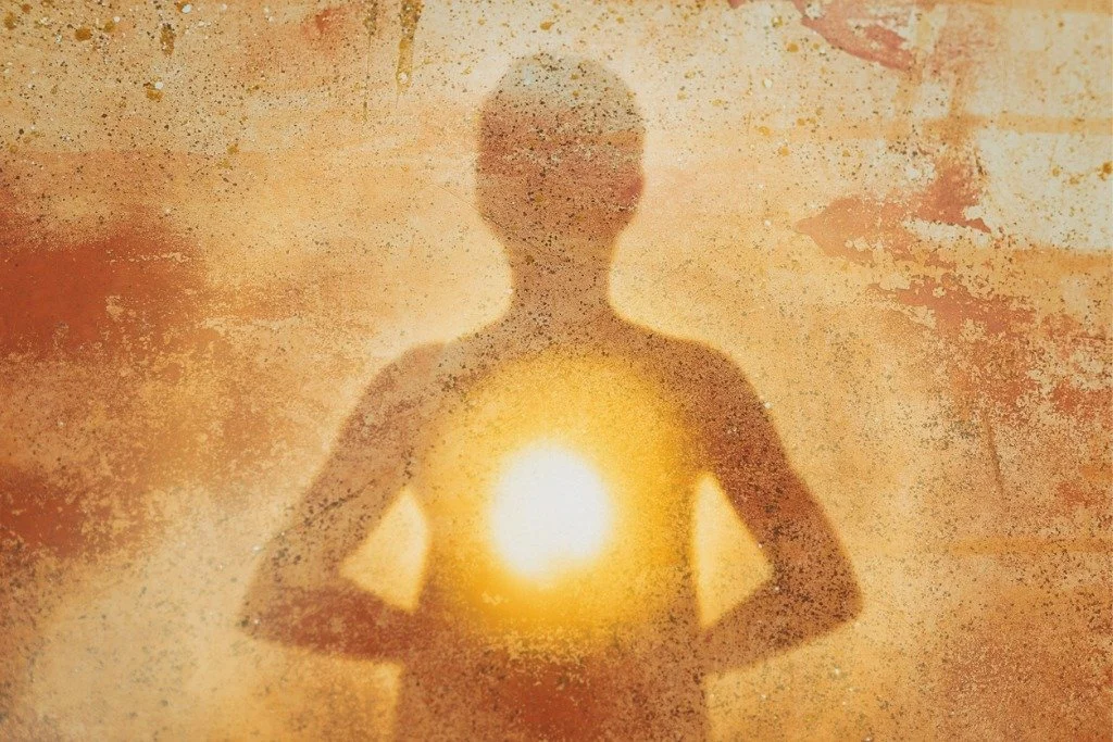 A silhouette of a person with a glowing bright light at the center of their chest, against an orange and textured background.