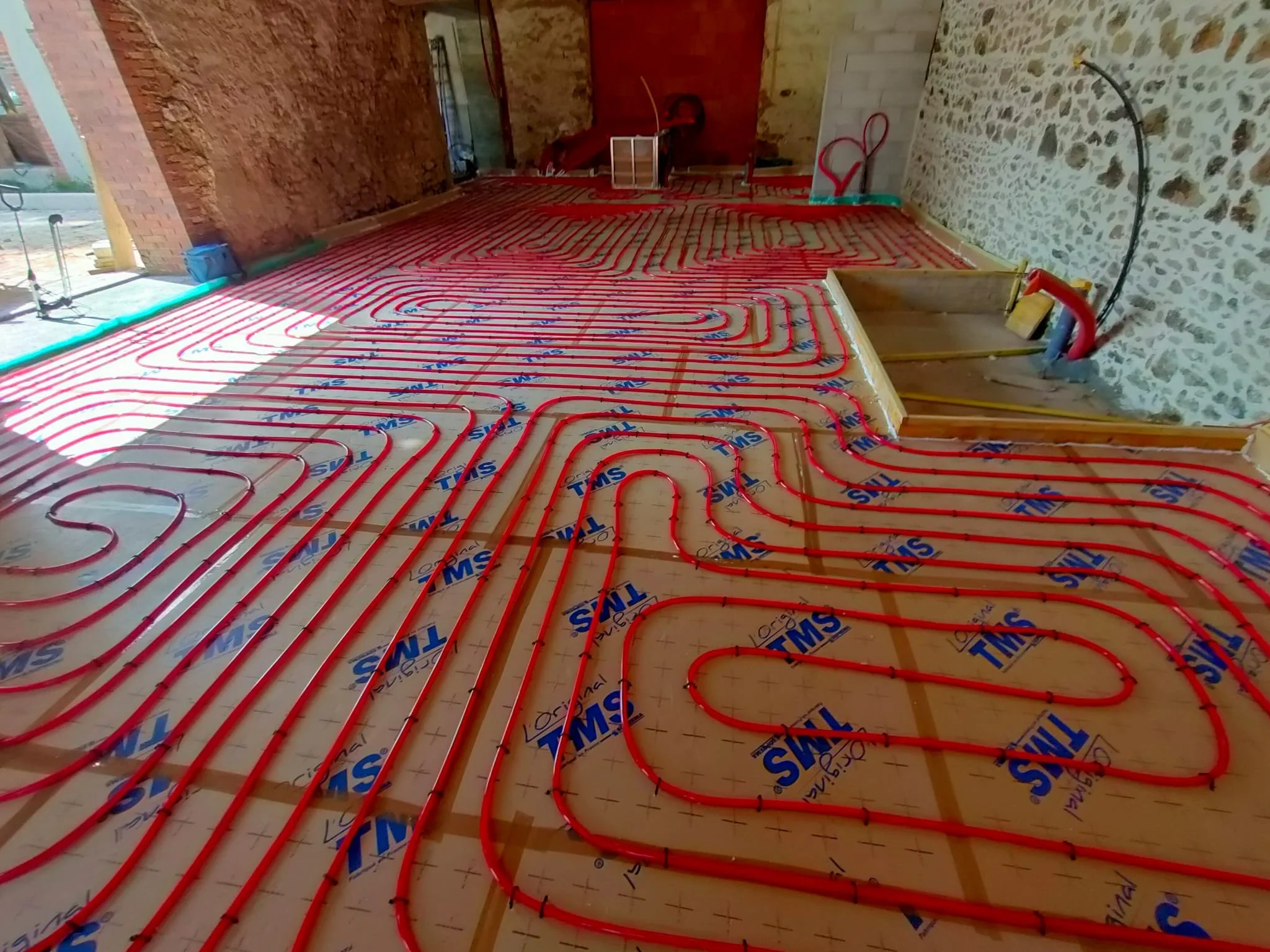Système de chauffage au sol en cours d'installation dans une pièce, avec des tubes rouges disposés en boucle sur le sol en préparation.