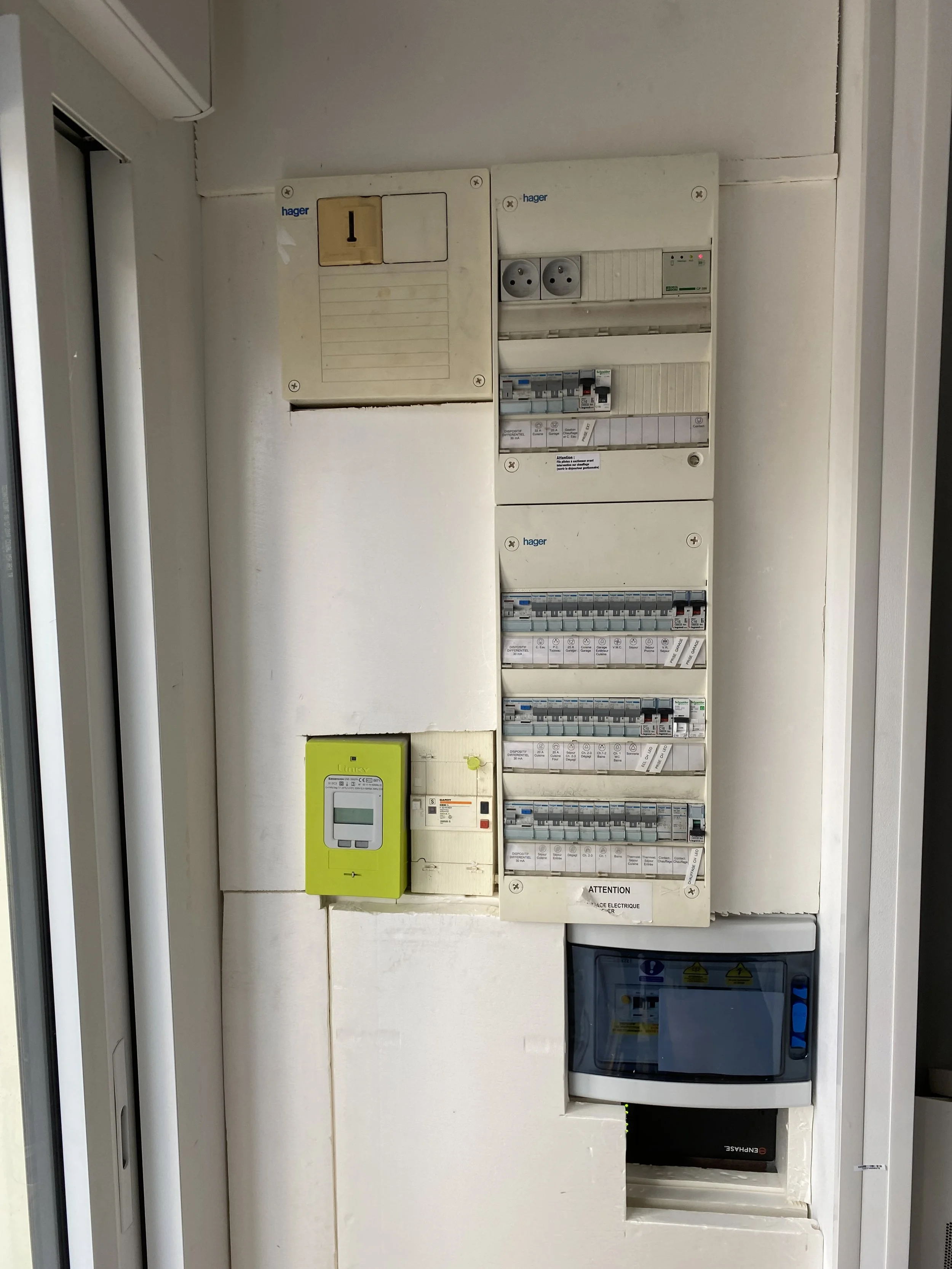 Panneau électrique avec plusieurs disjoncteurs et prises électriques, appareil vert de contrôle électrique, et un disjoncteur principal.