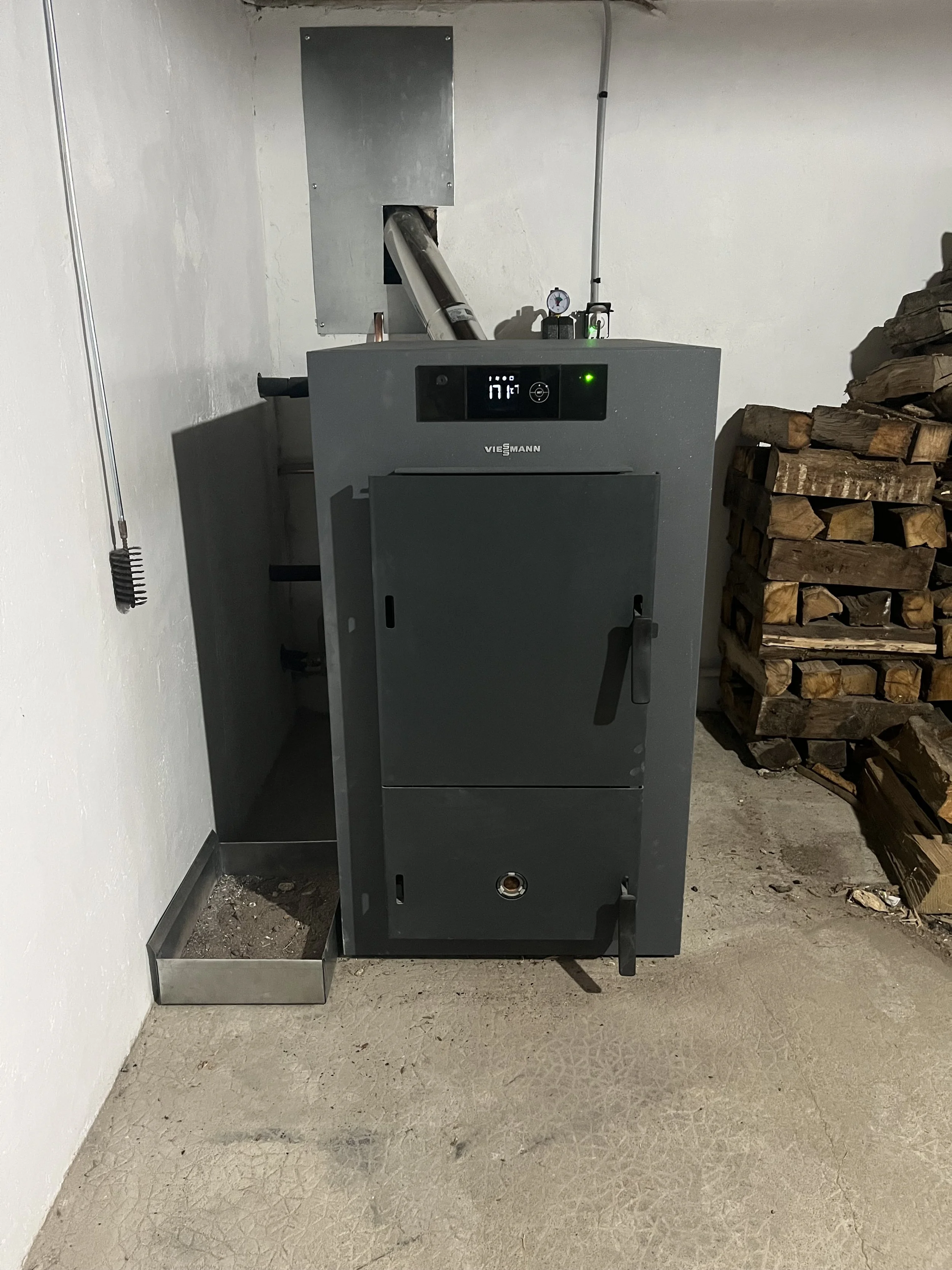Chaudière à huile vießmann dans une pièce avec bûches de bois empilées à droite.