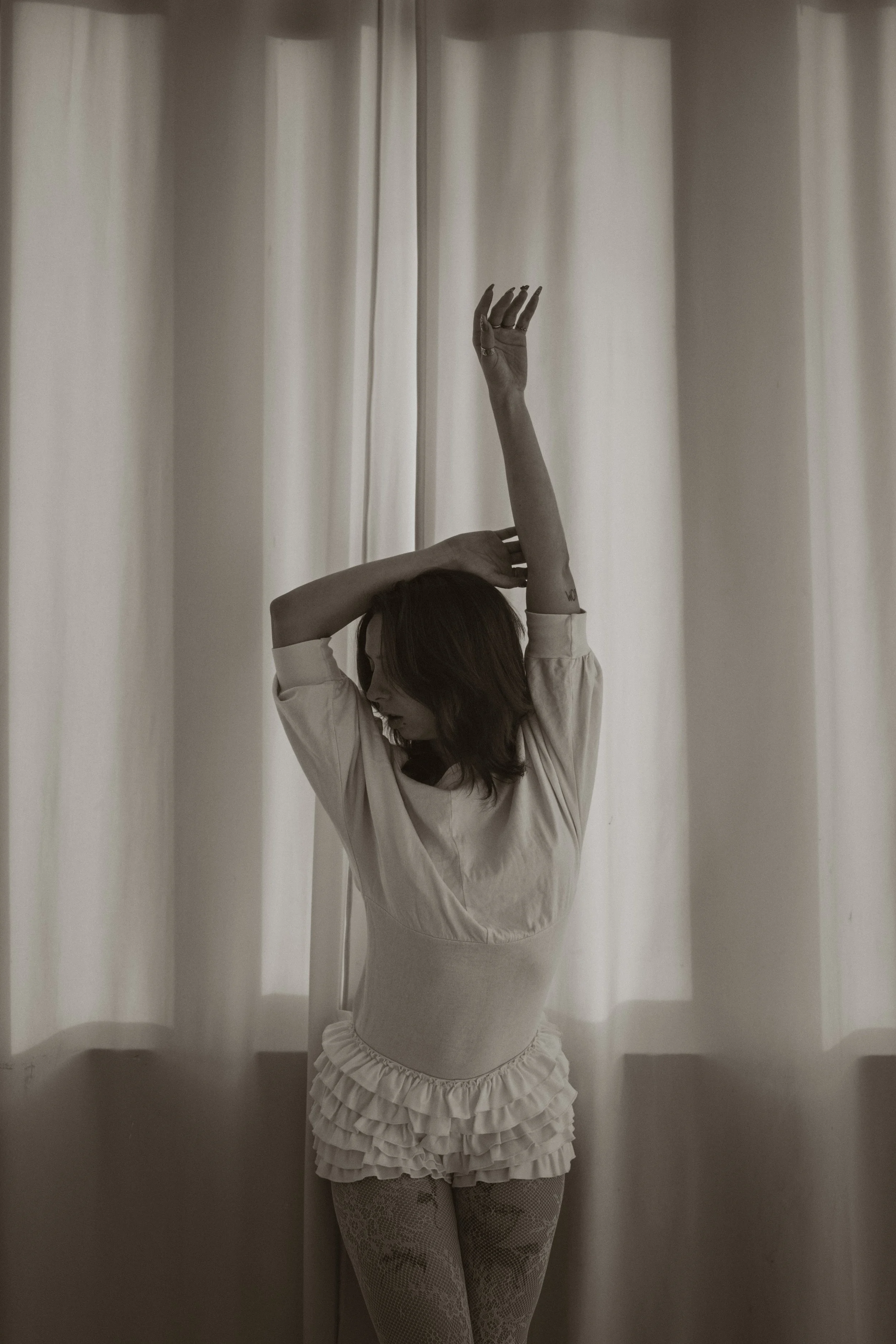Une femme en vêtements décontractés avec des bas en dentelle pose près d'un rideau blanc, avec une pose artistique.