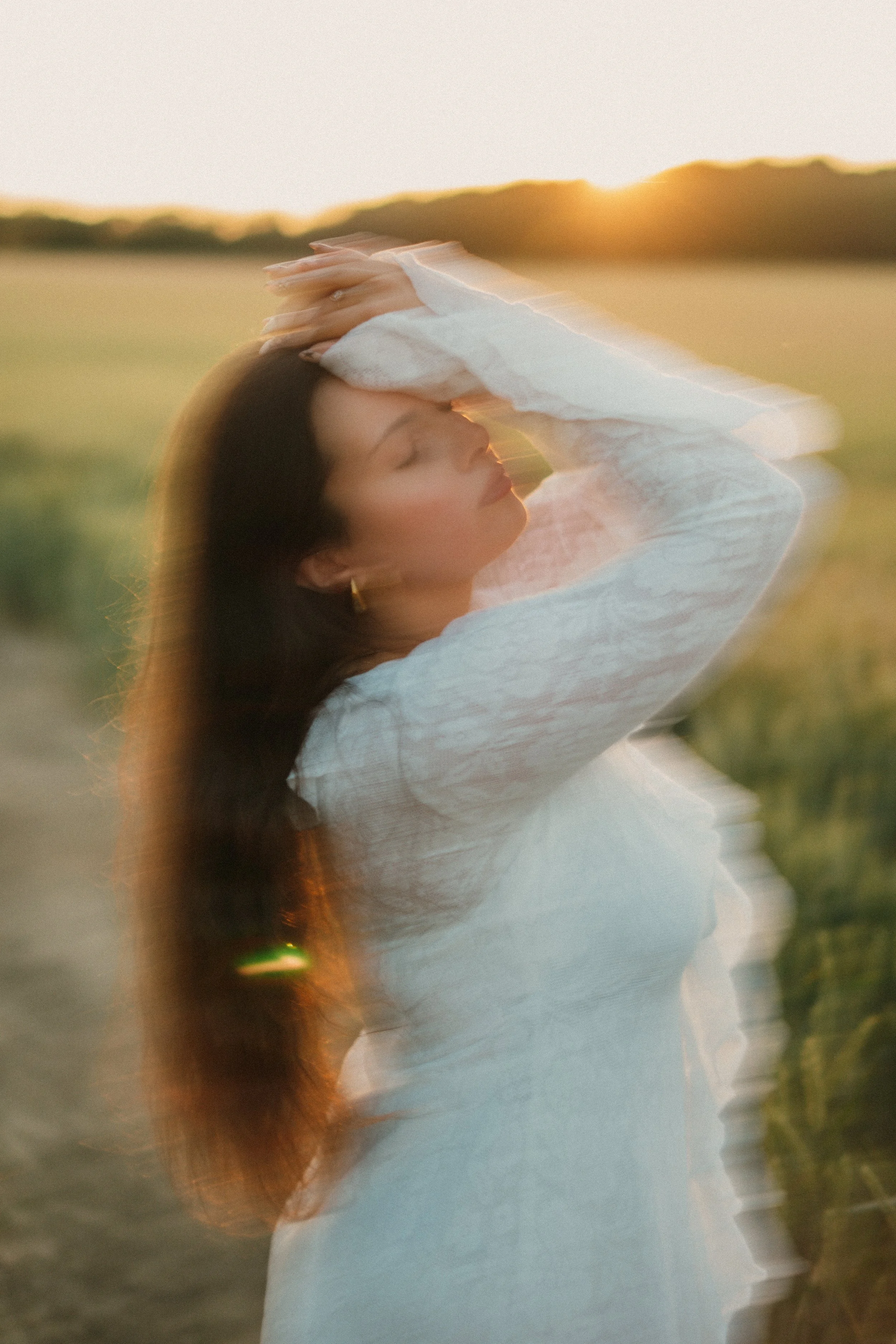 Jeune femme en robe blanche, en mouvement, lors d'un coucher de soleil dans un champ, avec flou artistique.