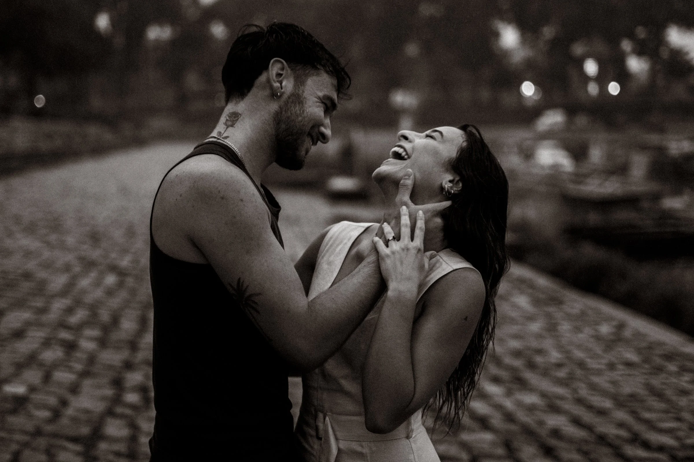 Un couple riant et s'amusant en plein air, se tenant face à face avec une ambiance joyeuse, en noir et blanc.