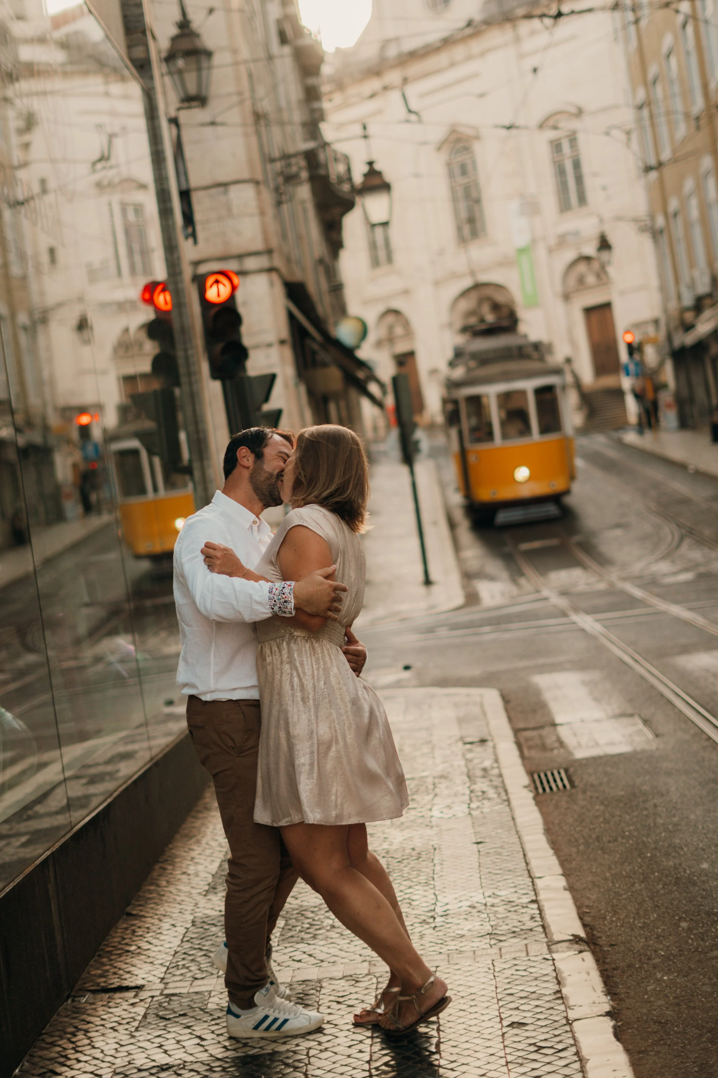 Un couple s'embrassent et se tiennent dans la rue pavée d'une ville européenne avec un tram jaune en arrière-plan.