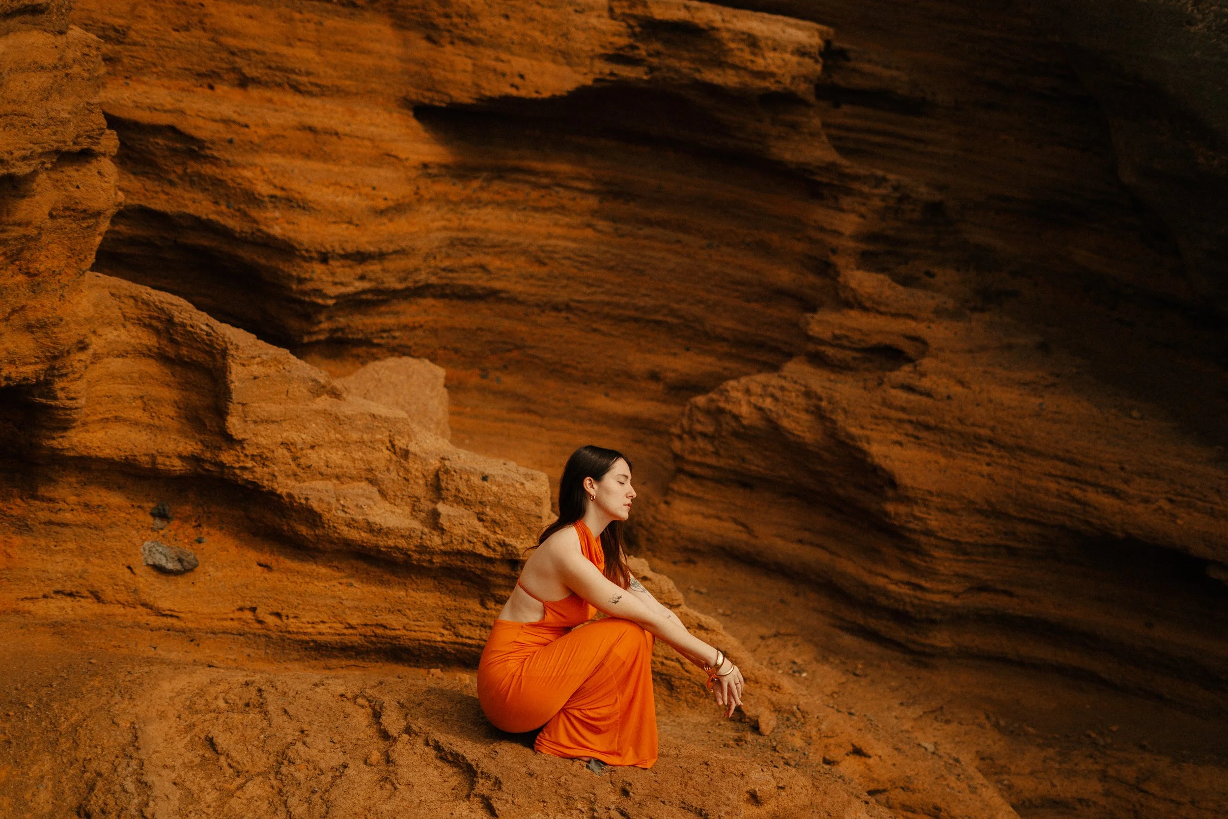 Femme assise en méditation dans un environnement rocheux de couleur orange.