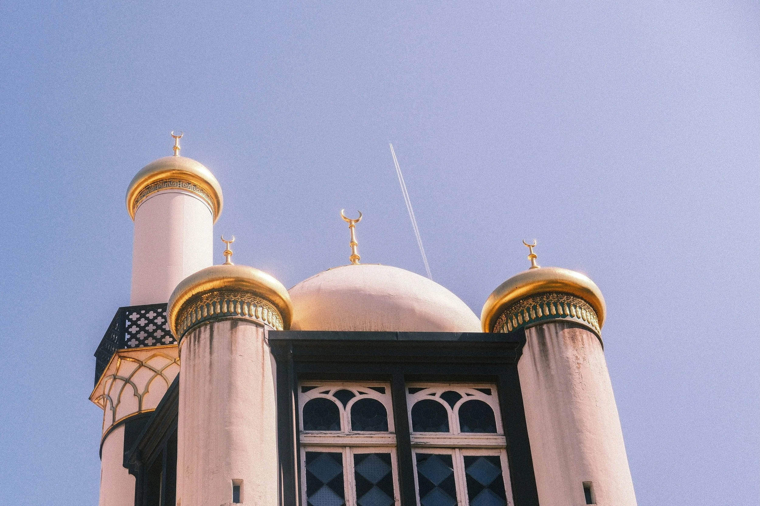 Blick auf die goldenen Kuppeln und Türme eines islamischen Minaretts vor einem klaren blauen Himmel.