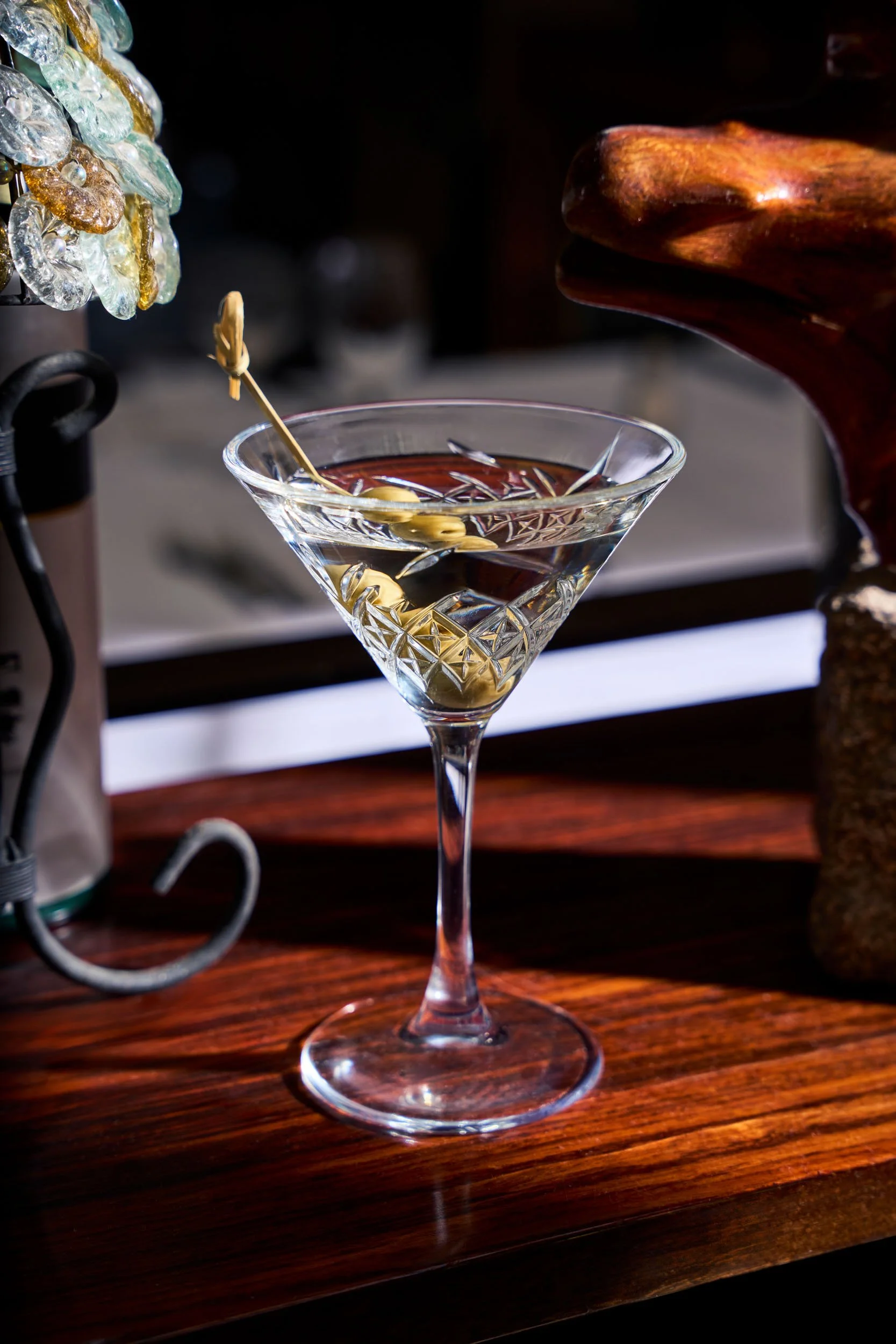 Un cocktail trasparente servito in un bicchiere da martini con un'oliva e una scorza di limone, decorato con uno stecco