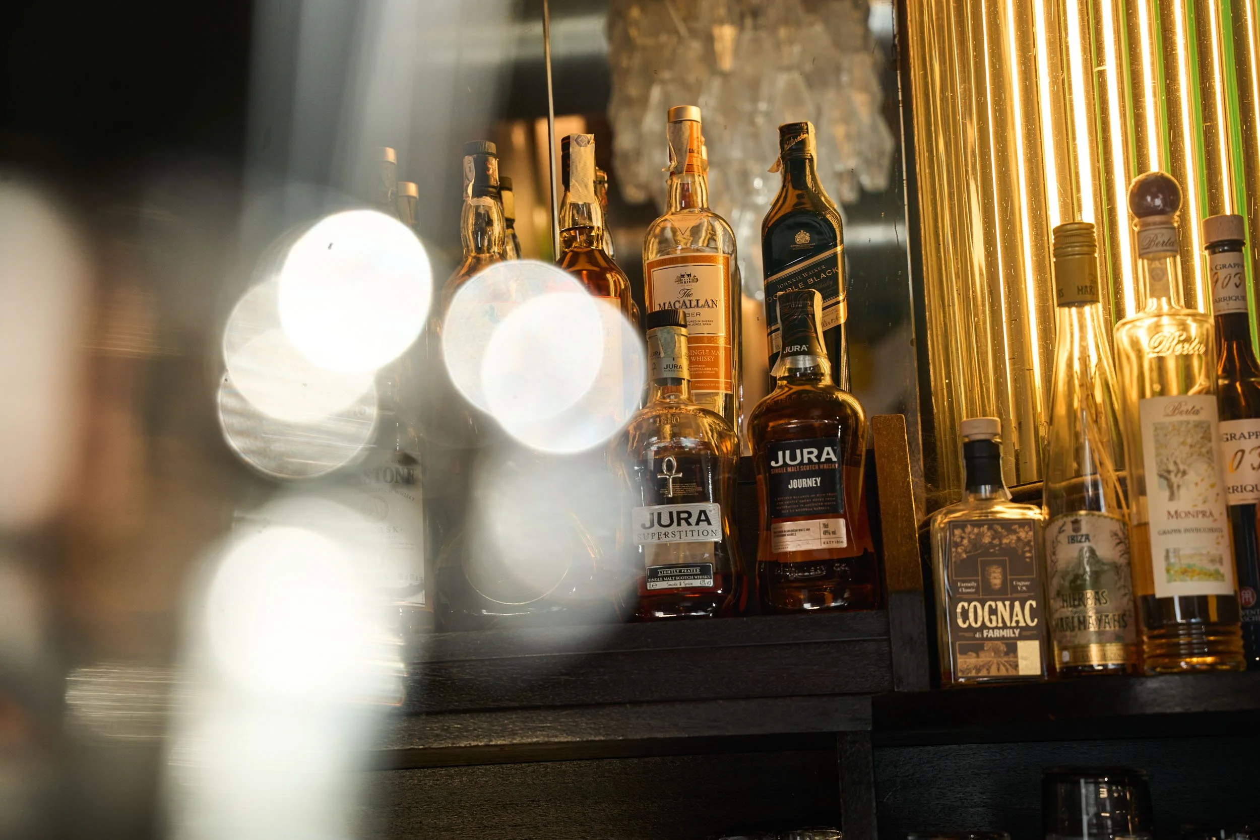 Scaffale con bottiglie di liquor e whisky, tra cui Jura, Macallan e Cognac, in un bar.