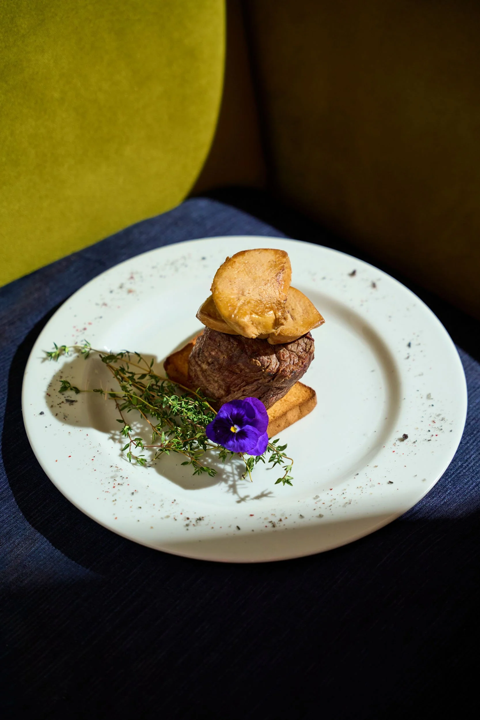 Piatti di carne con patate e una pianta aromatica decorativa, tutto su un piatto bianco.