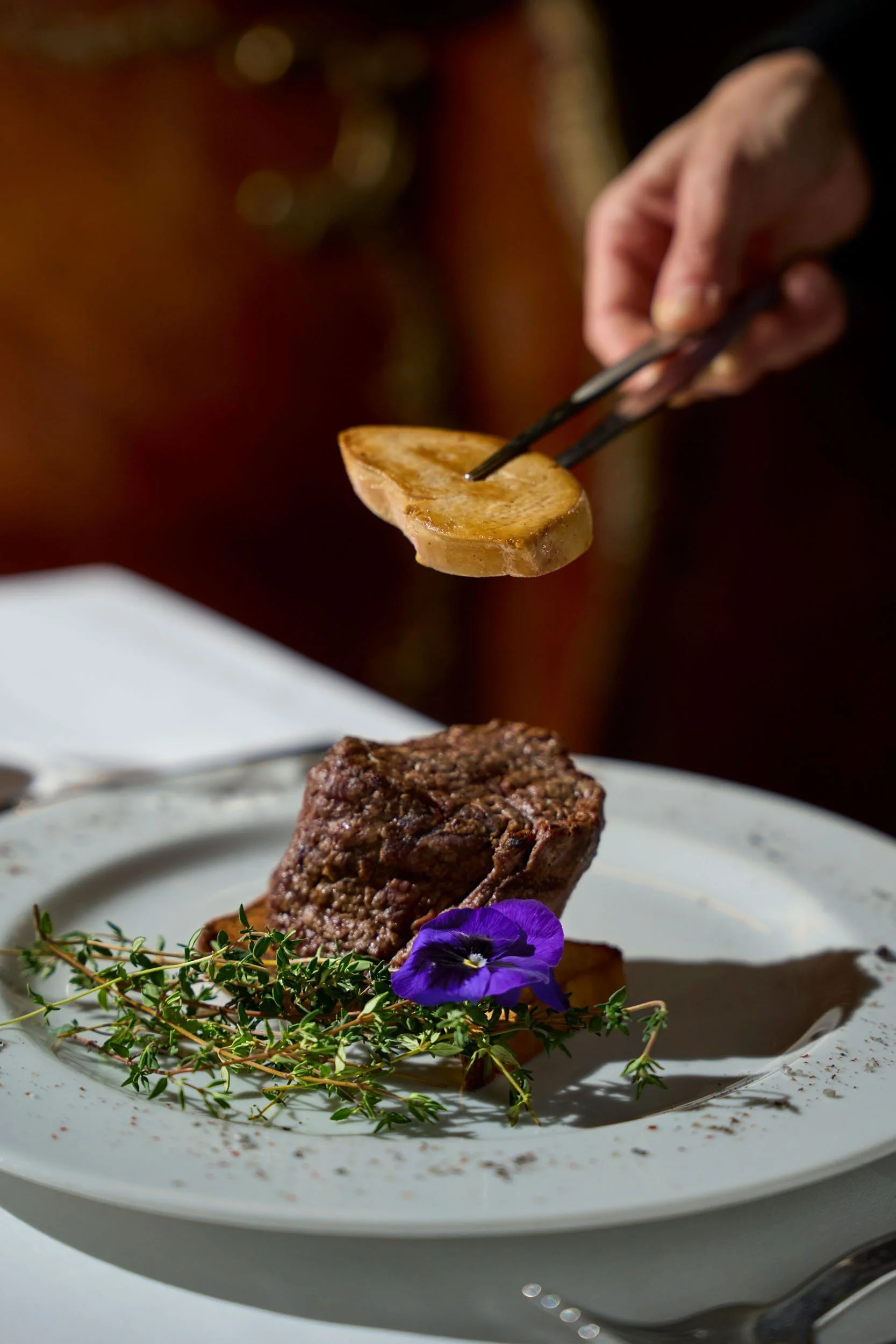 Carne rossa cotta con un fiore viola e foglie verdi decorativi su un piatto bianco.