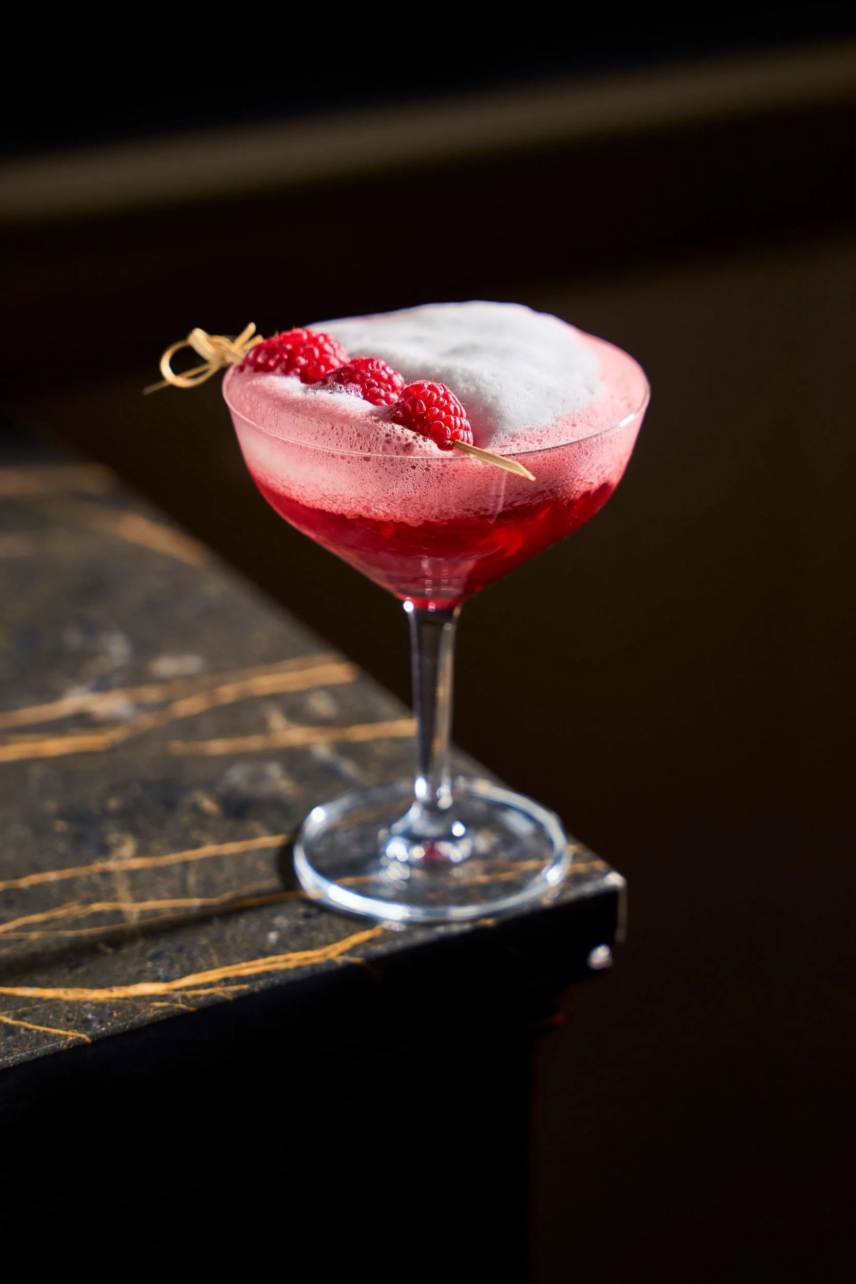 Cocktail rosso con schiuma bianca e lamponi come decorazione, in un bicchiere da cocktail su un bancone di marmo scuro