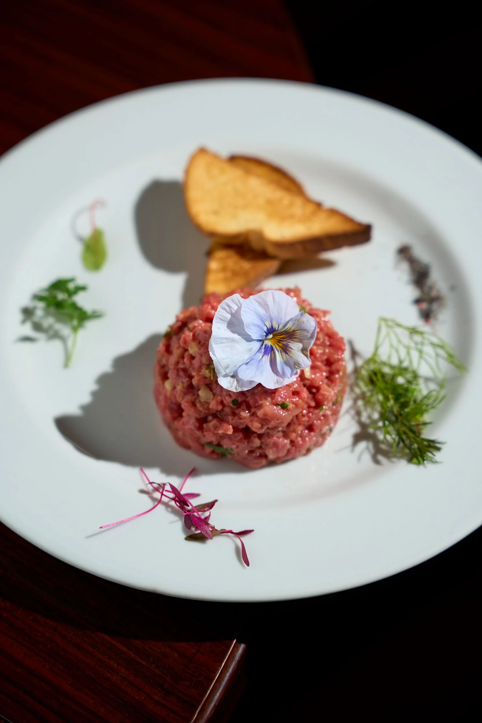 Tartare di carne con fiore ed erbe aromatiche, accompagnato da due fette di pane tostato.
