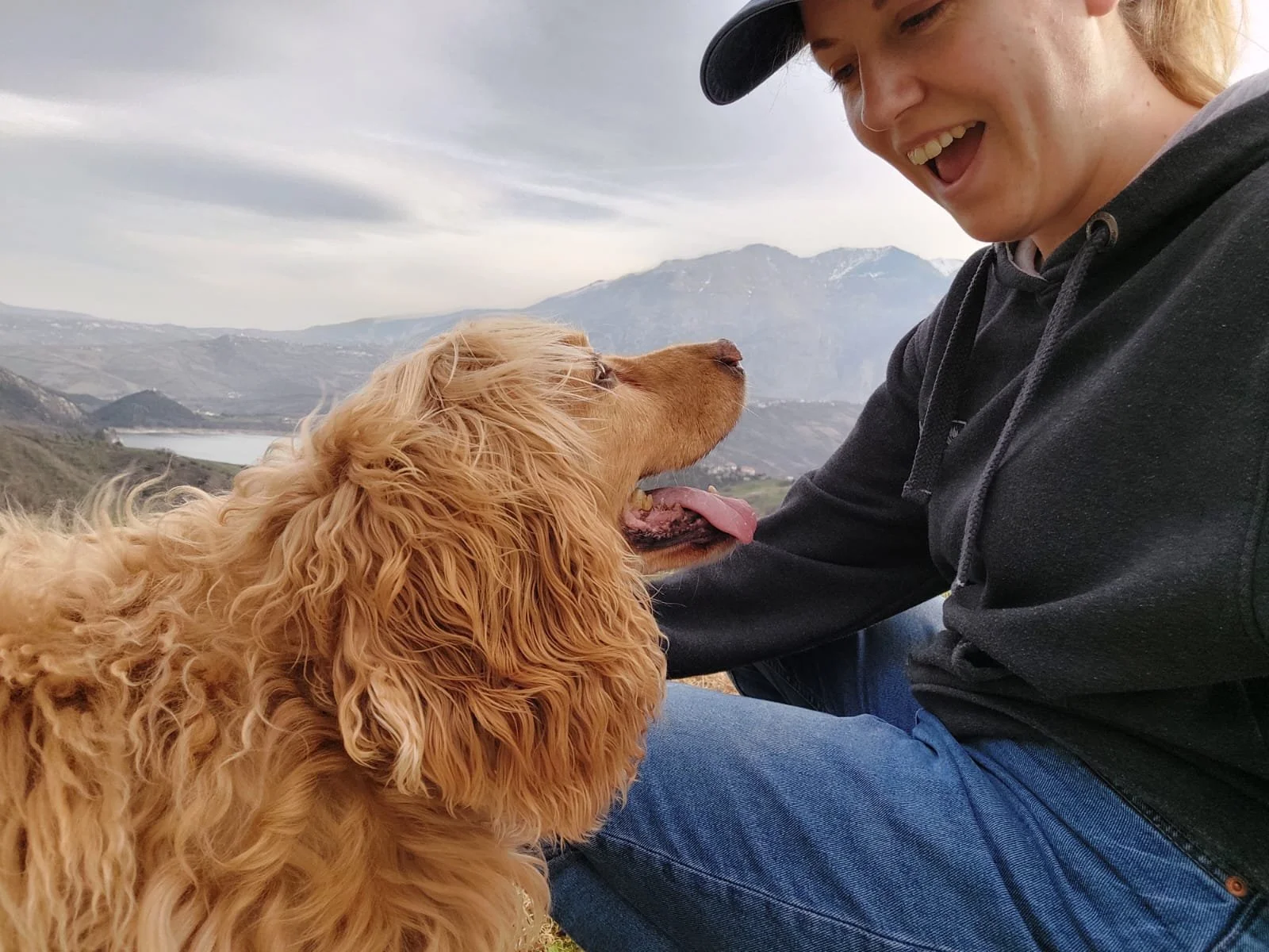 A woman and a golden cockerspaniel dog enjoying outdoors with mountains in the background.