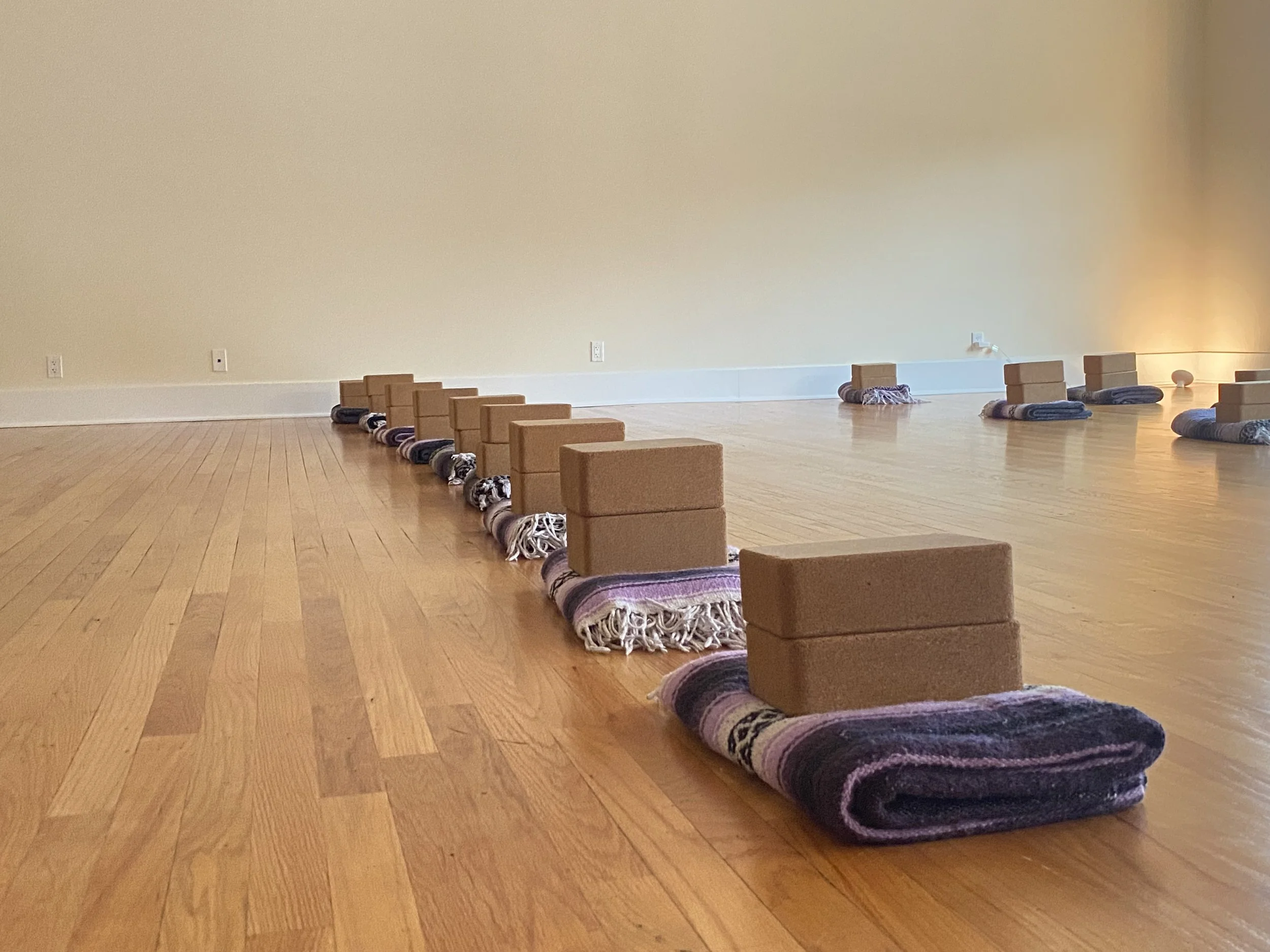 Yoga mats with blocks arranged in a line on a wooden floor in a spacious, empty room.