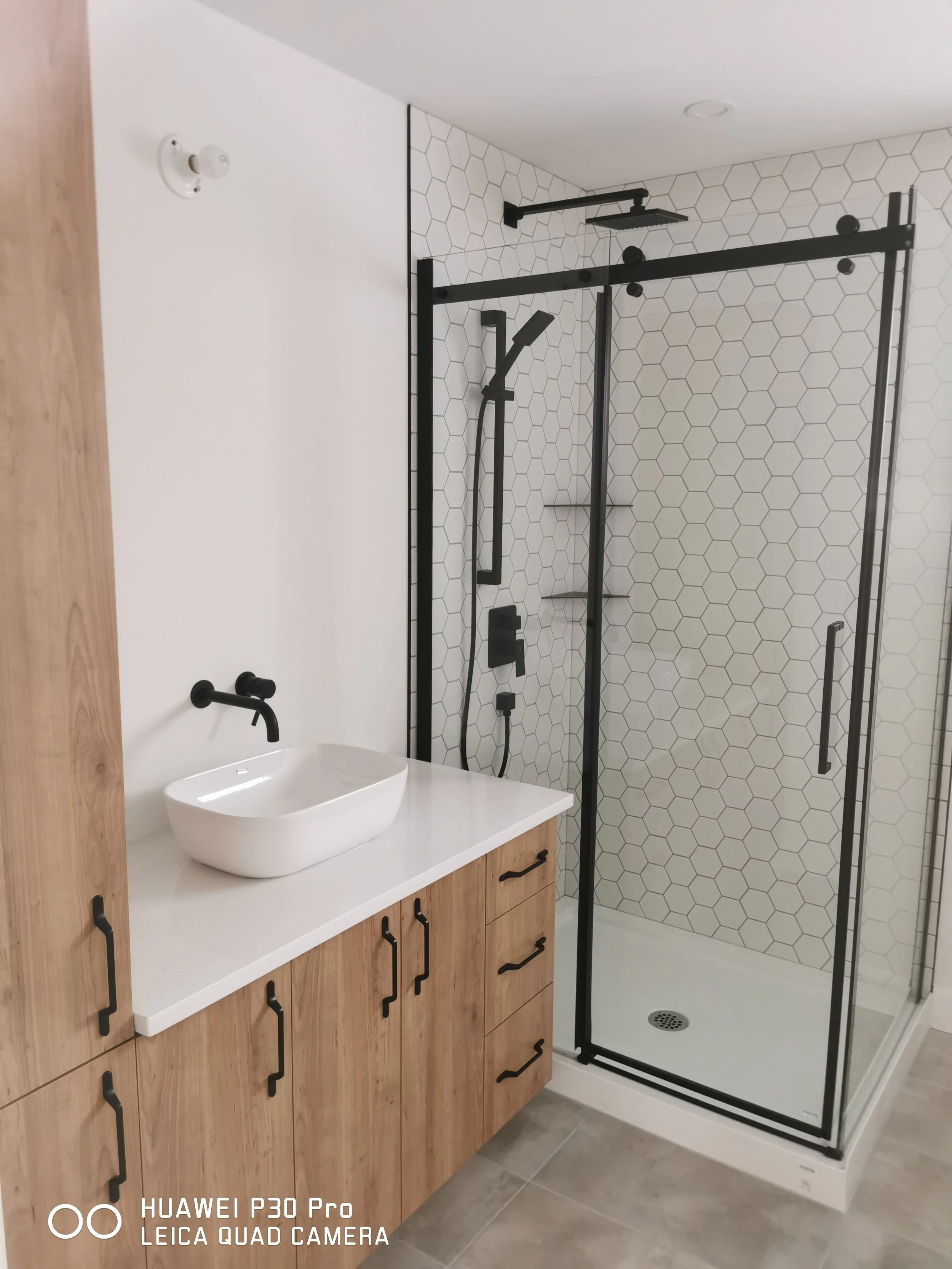 Salle de bain blanche avec un évier et une douche vitrée réalisée par Groupe Corripresto à Sorel-Tracy