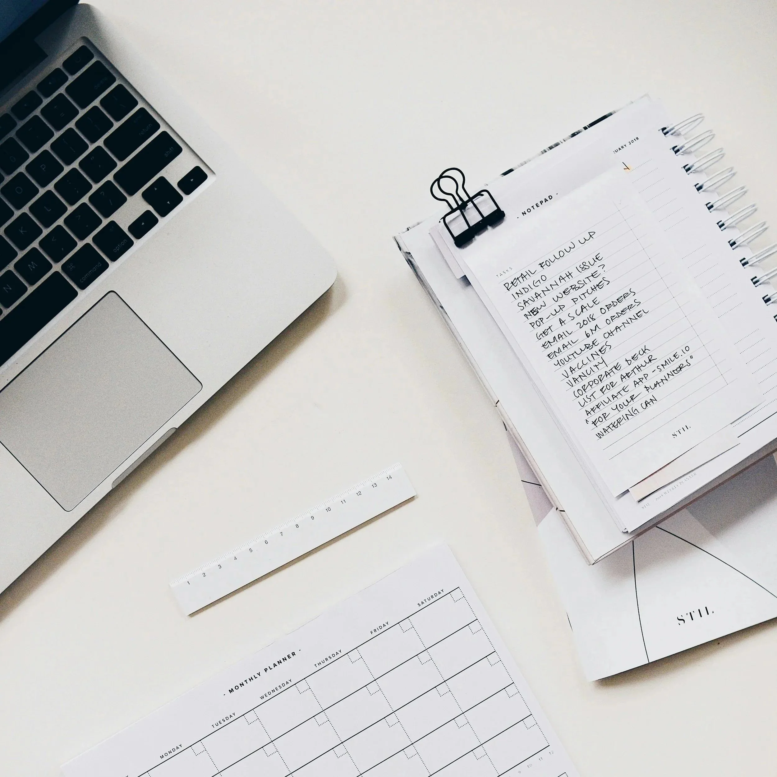 Un bureau avec un ordinateur portable, un calendrier ouvert avec des notes écrites à la main, et une règle.
