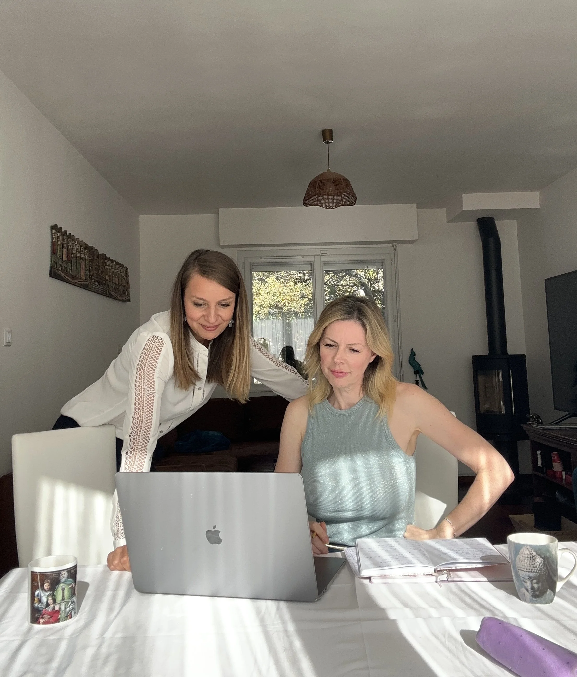 Deux femmes regardant un ordinateur portable sur une table dans une pièce lumineuse.