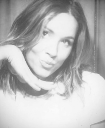 Black and white photo of a woman with shoulder-length hair making a playful kiss face with her lips puckered and her hand near her chin.
