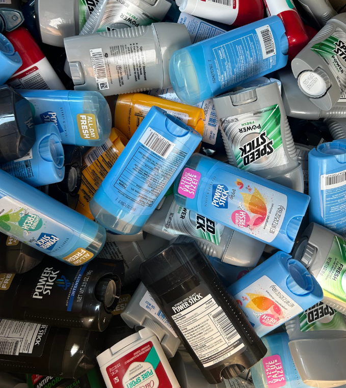 A pile of mostly blue, black, green, red, yellow, and white bottles of personal care products, including spray and pump bottles, with labels showing brands like Speed Stick and Old Spice.