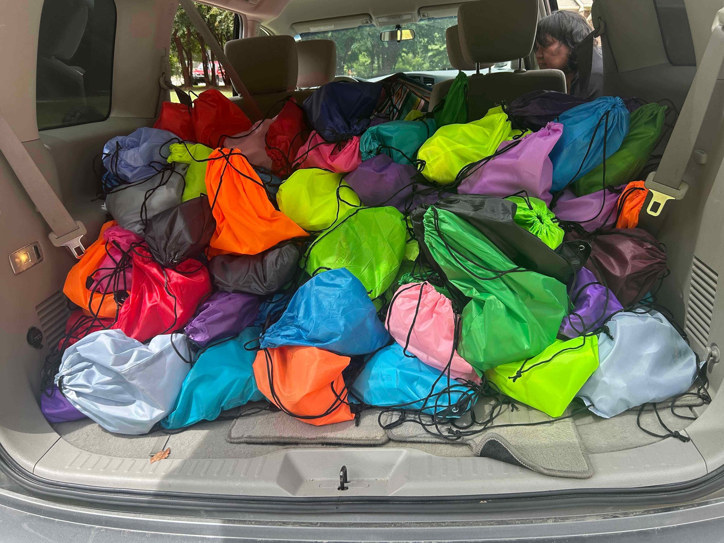The back of a vehicle filled with numerous colorful drawstring bags in various colors, including orange, red, blue, green, purple, pink, gray, and black.