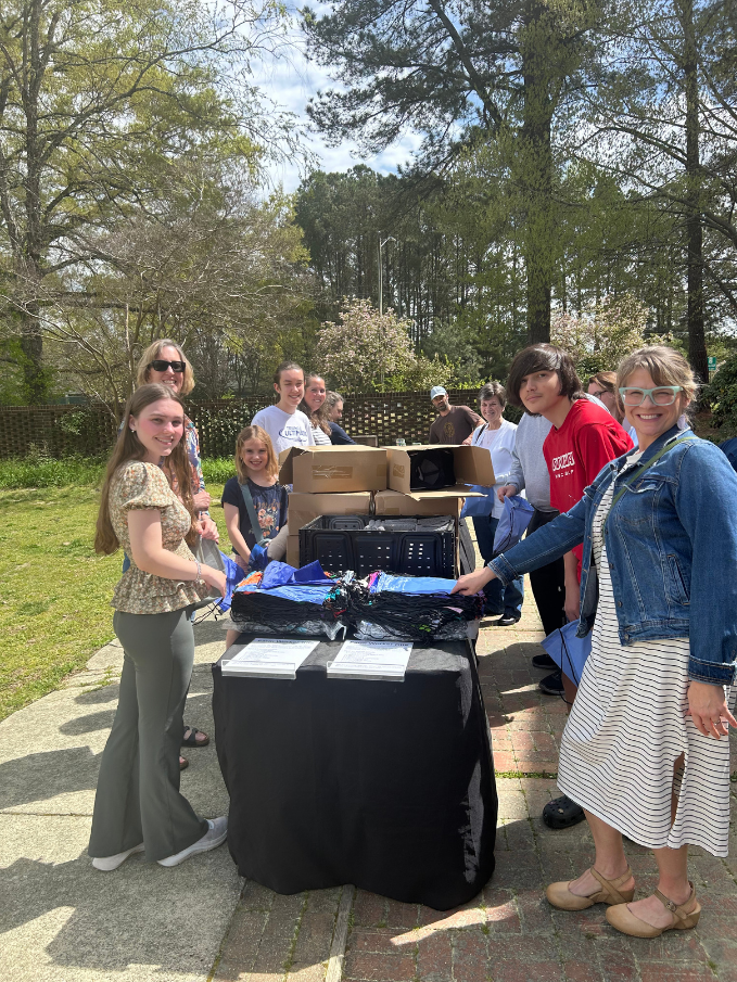 Group of people gathered around a table with items for distribution outdoors on a sunny day with trees in the background.