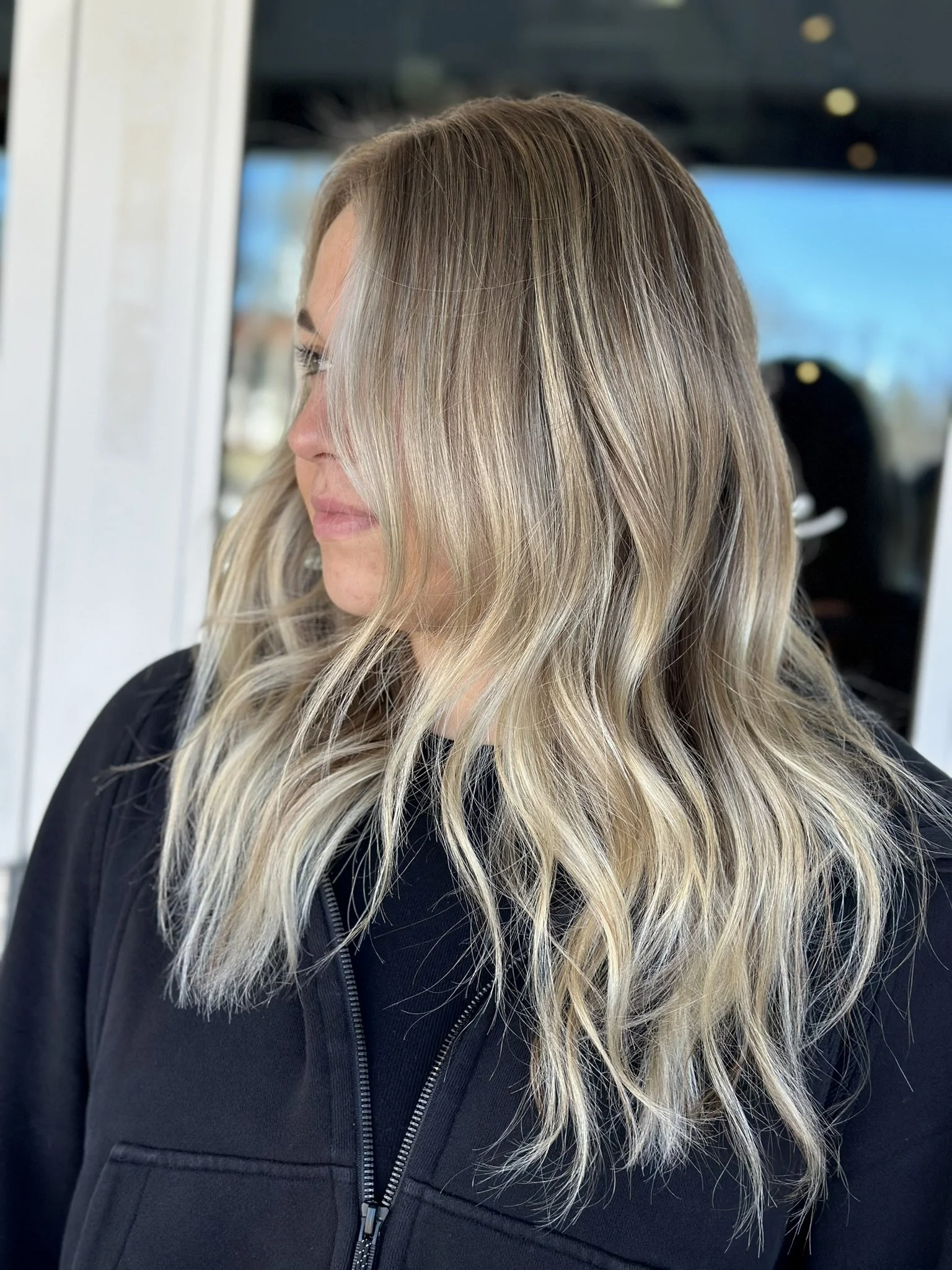 Woman with wavy, blonde hair wearing a black zip-up jacket.