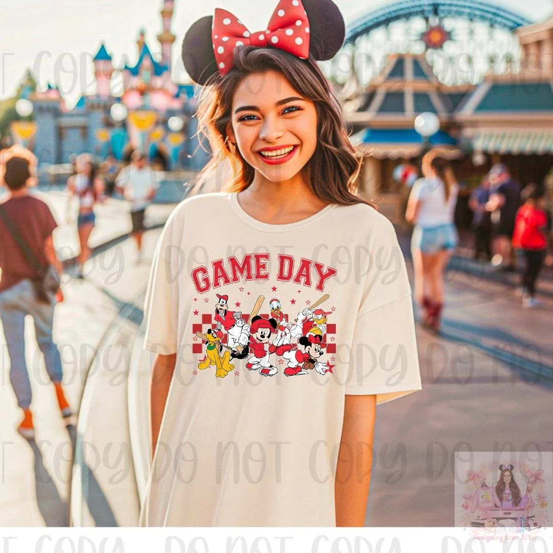 A young woman with long brown hair, wearing red lipstick, Minnie Mouse ears headband, and a beige T-shirt with 'Game Day' and Disney characters on it, at an amusement park.