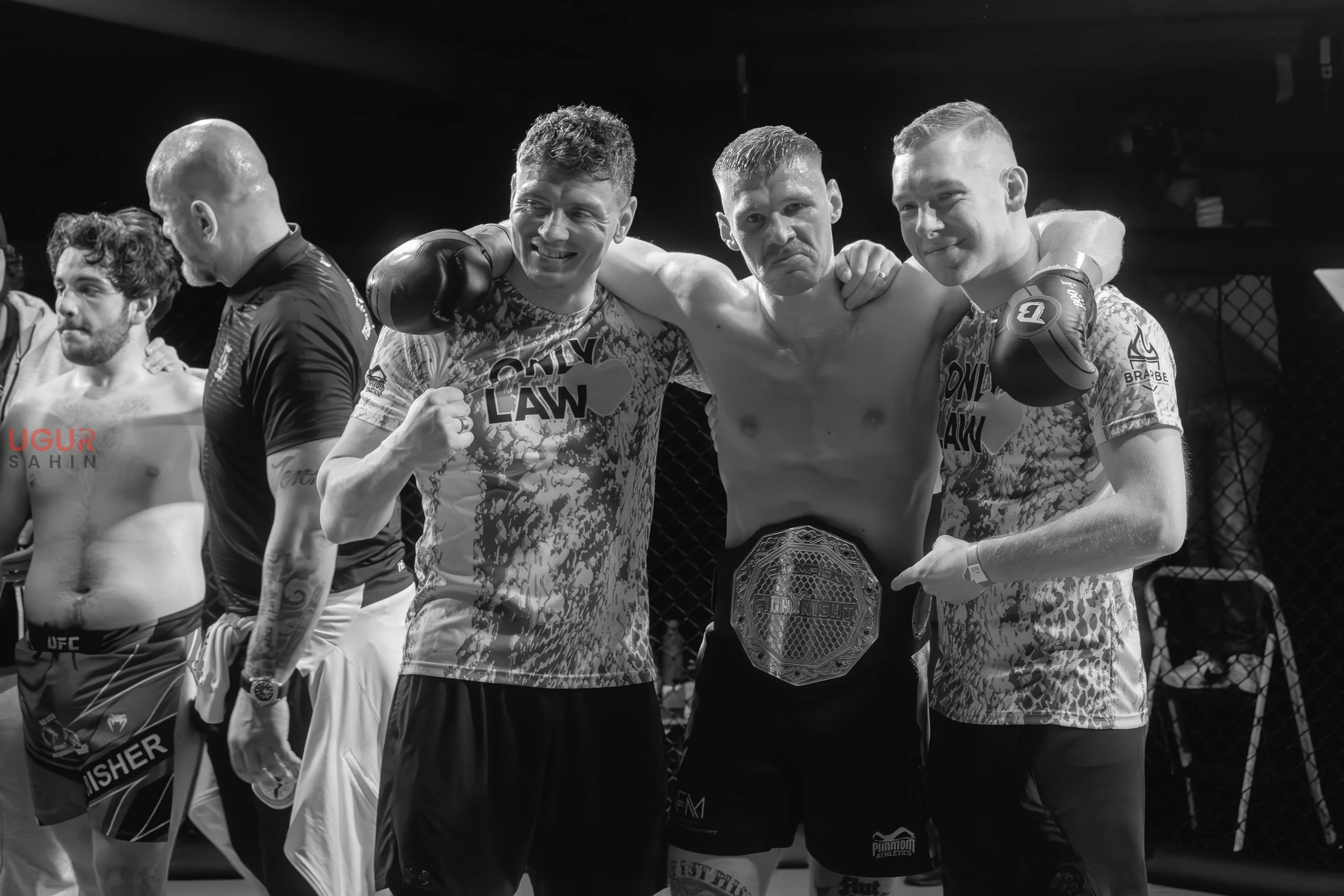 Sieger im Mixed Martial Arts Kampf, drei Kämpfer im Käfig, einer mit Medaille, feiern den Sieg, schwarz-weiß Fotografie.