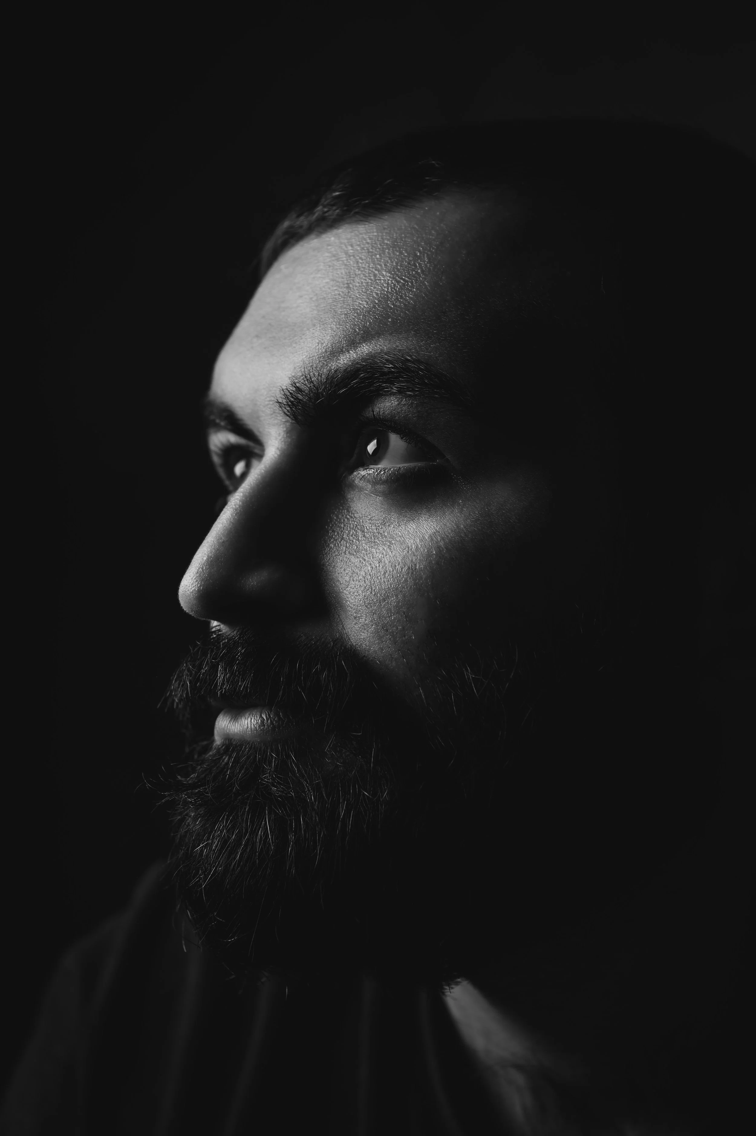 Schwarz-weiße Nahaufnahme eines Mannes mit Bart und glattem Haar, der nach rechts blickt.