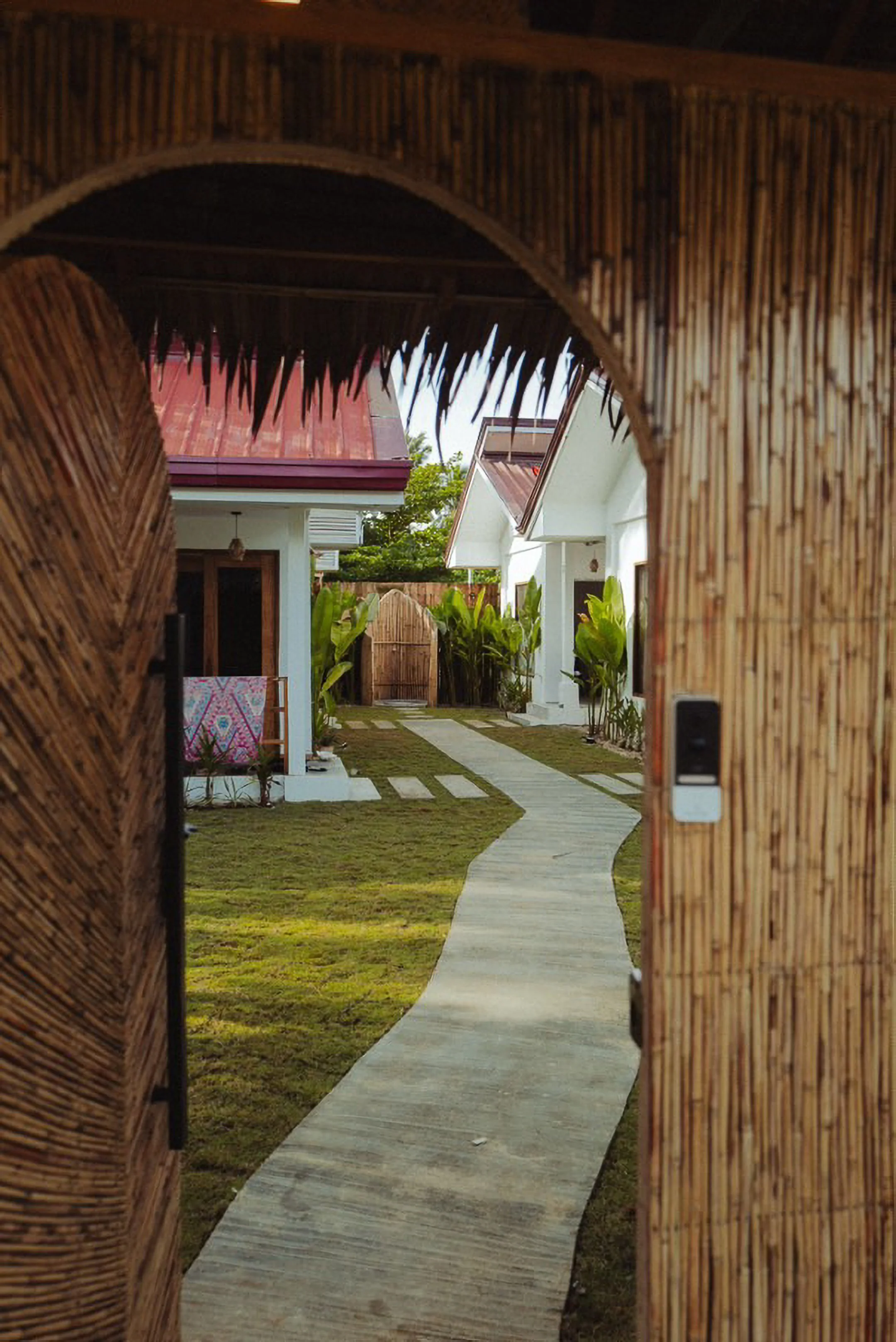 White Palm Villas Siargao entrance with bamboo gate opening to a curved pathway leading to tropical private villas surrounded by greenery
