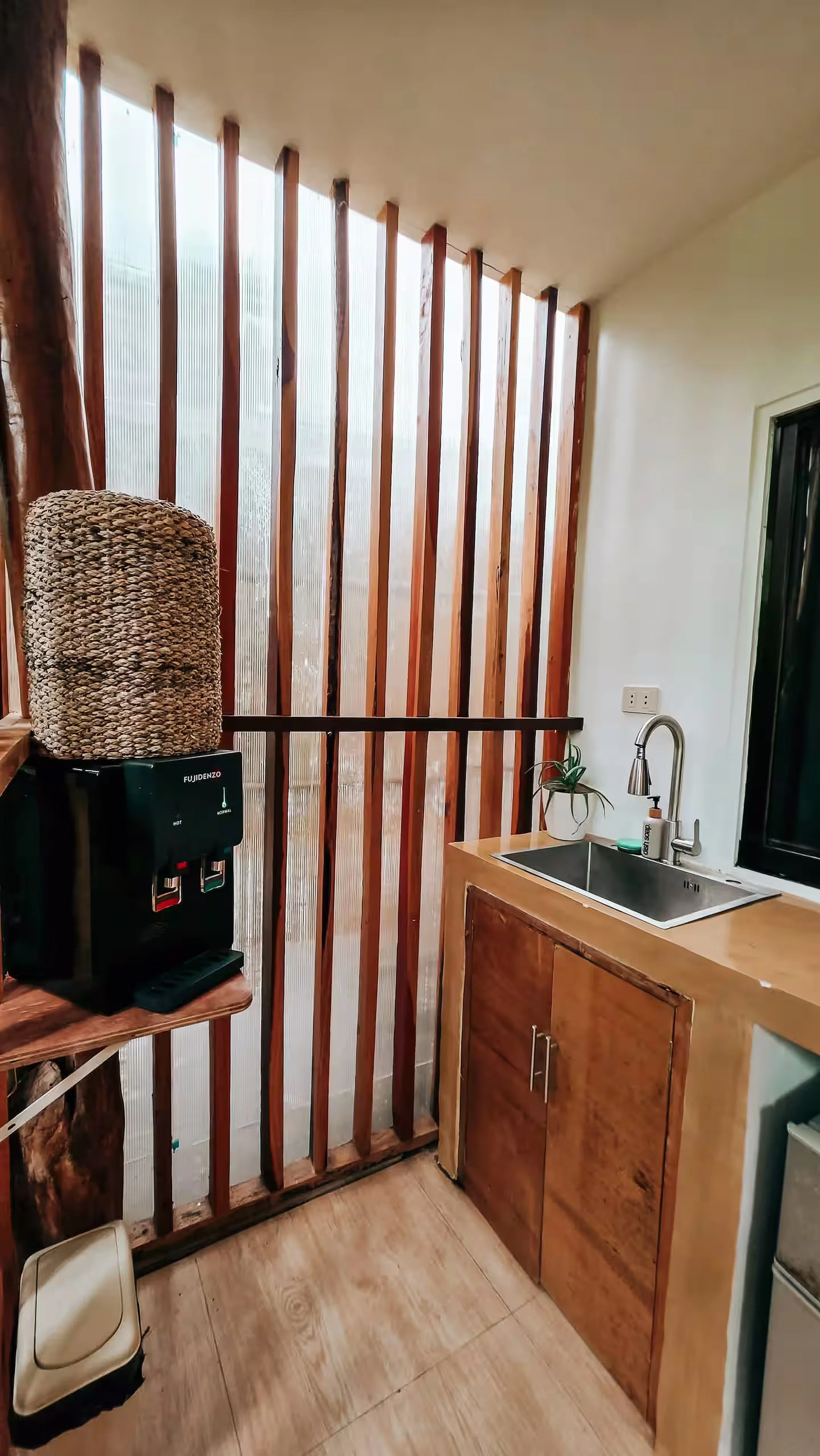 A view of the outdoor kitchen in Surf & Chill Room 3, featuring a stainless-steel sink, water dispenser, and natural wooden accents that create a bright and airy space for simple island cooking.