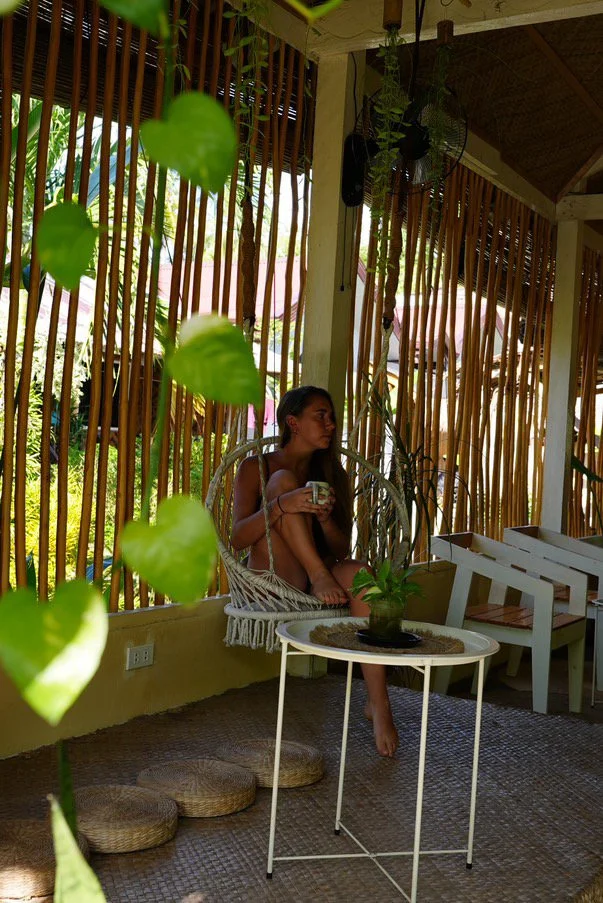 Surf and Chill Siargao chill space with a guest sitting in a hanging chair holding coffee in a relaxed tropical common area with natural light