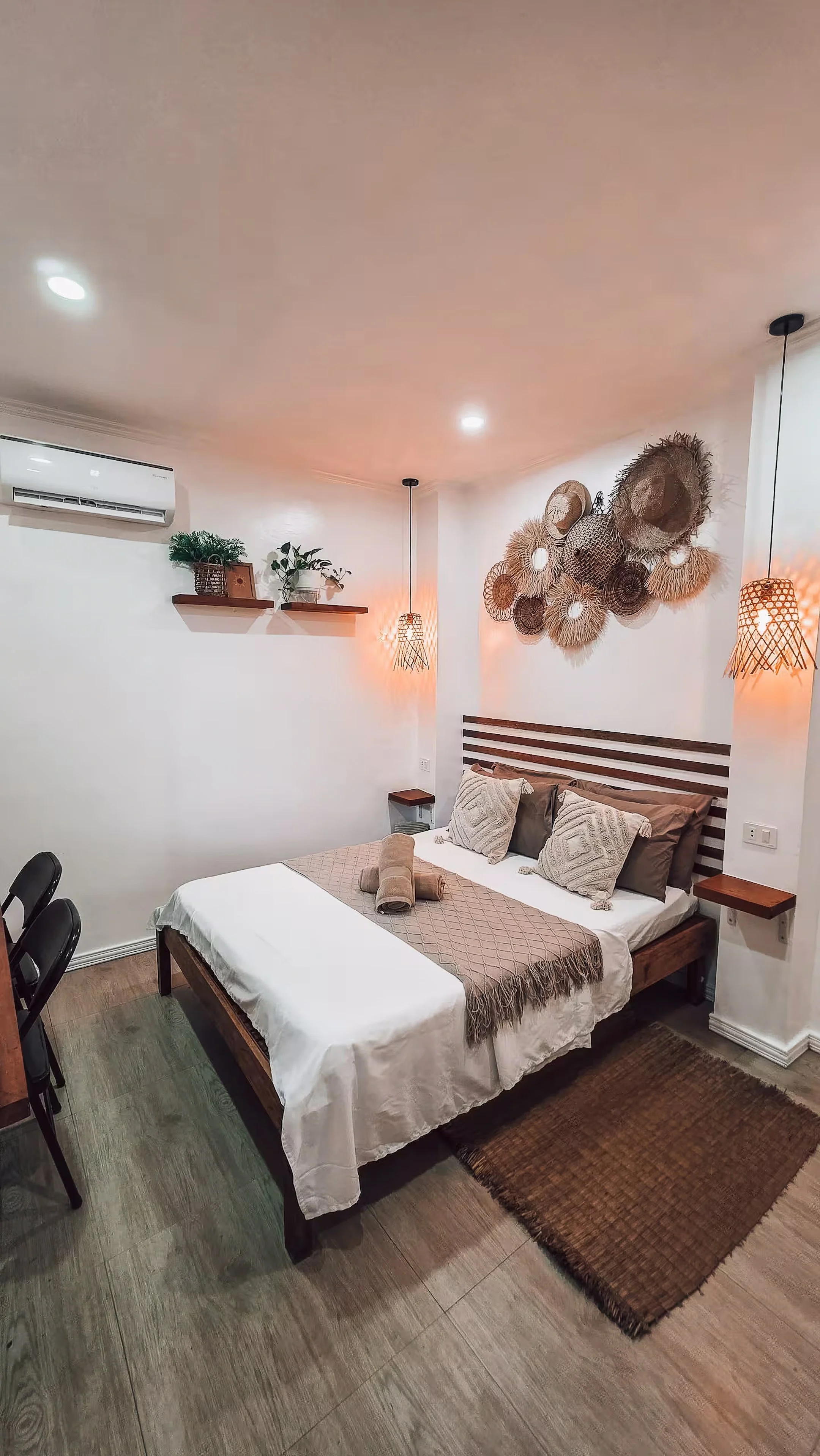A serene view of Surf & Chill Room 3 featuring a double bed, soft neutral tones, woven wall décor, and pendant lights that create a calm, coastal atmosphere ideal for relaxing after a day on the island.