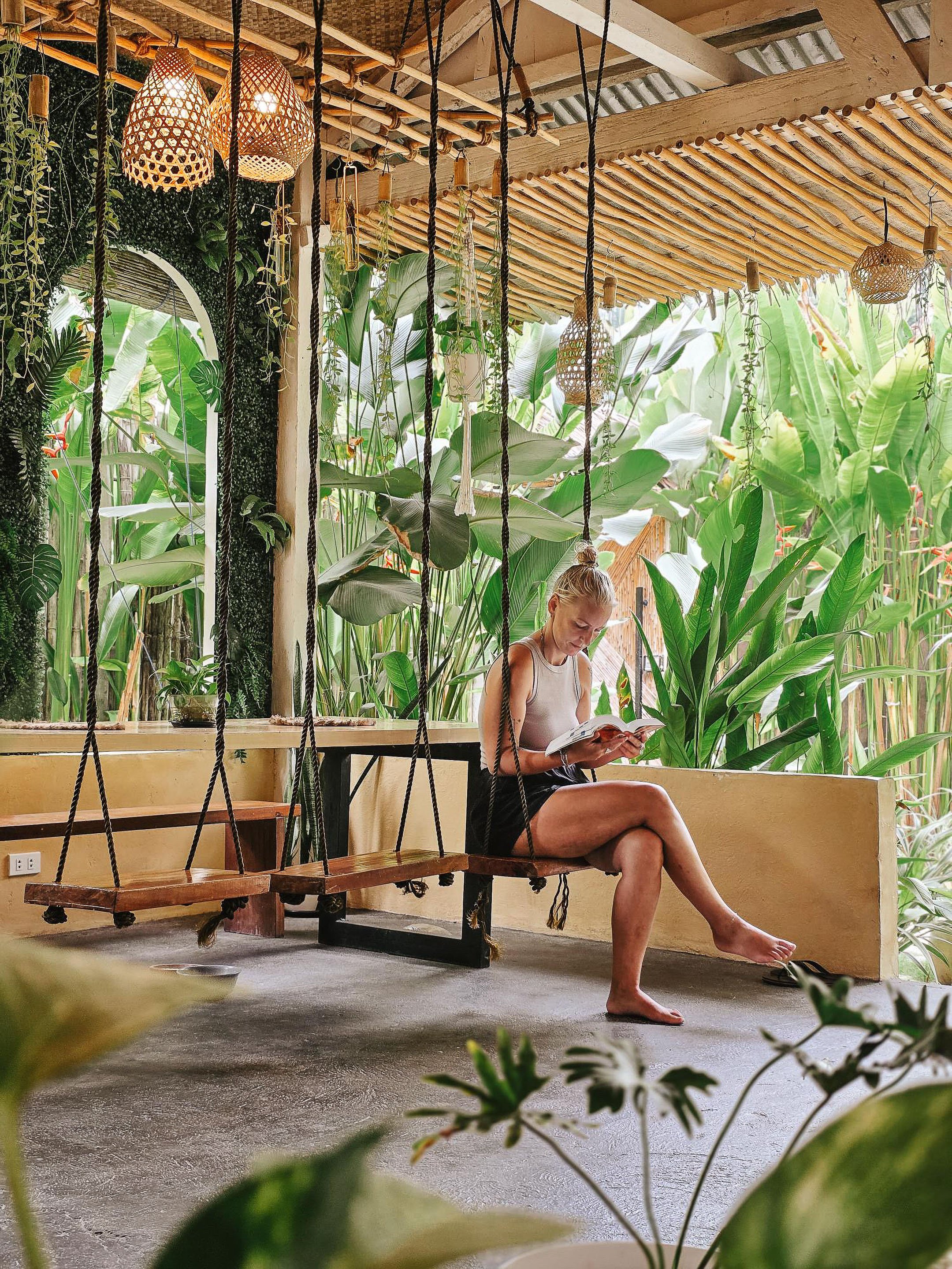 Surf and Chill Siargao chill space with hanging swing seating and a guest reading in an open-air tropical common area surrounded by greenery