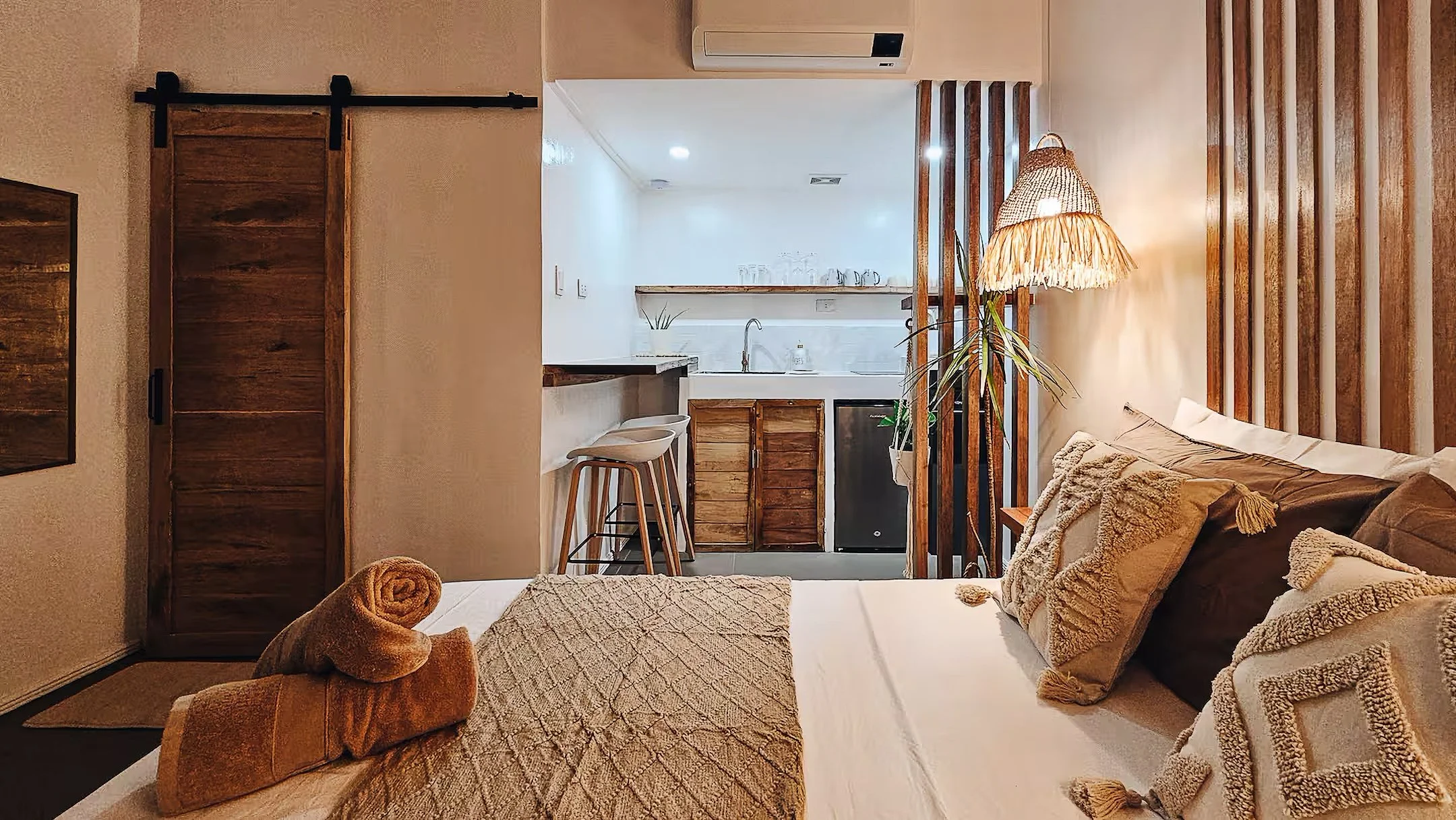 Cozy bedroom in Room 2 at Surf & Chill Siargao with a kitchenette, rattan lighting, and wooden accents.