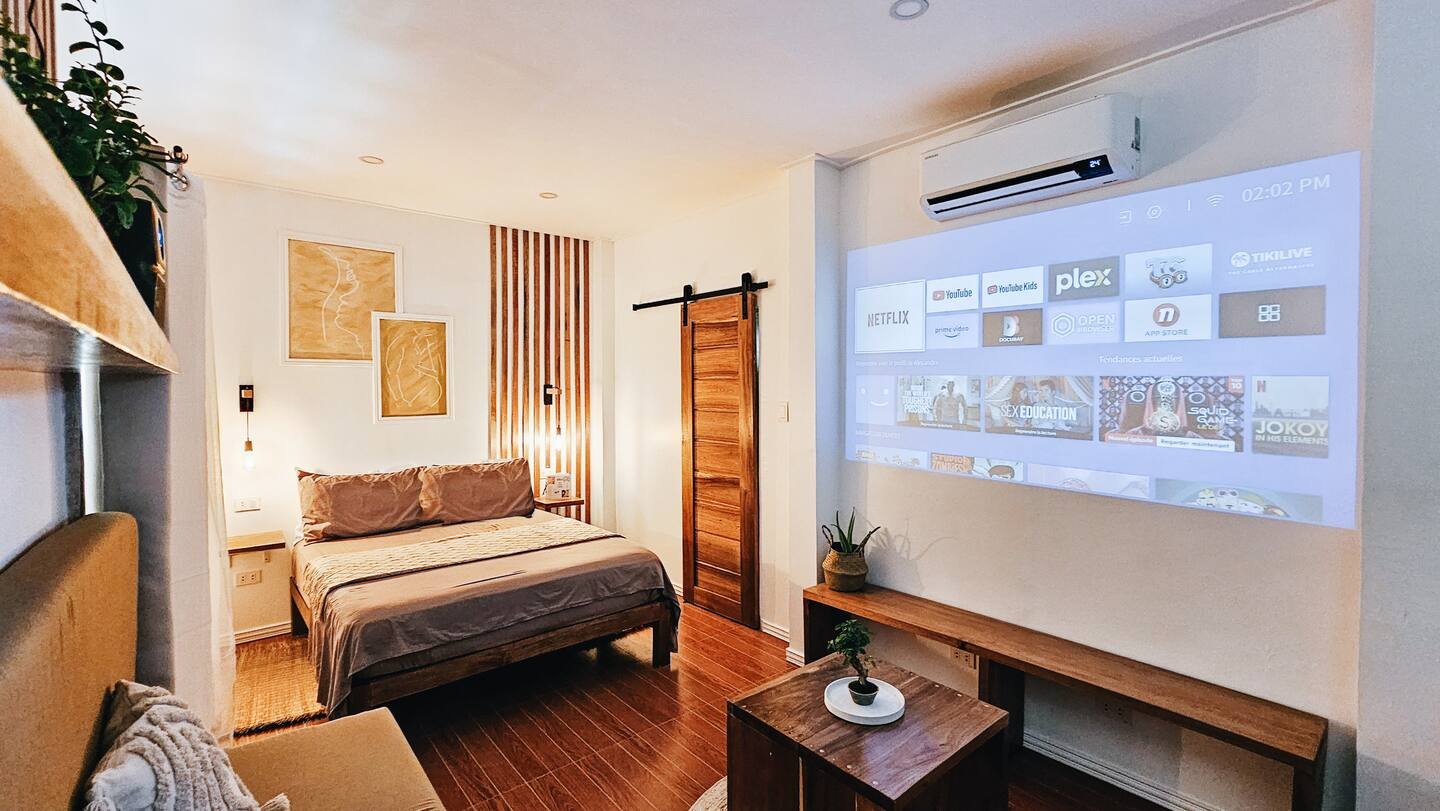 Cozy guest room at Surf and Chill Siargao in Catangnan, General Luna featuring a queen-sized bed, Smart Projector setup with Netflix, wooden interiors, and modern tropical design.