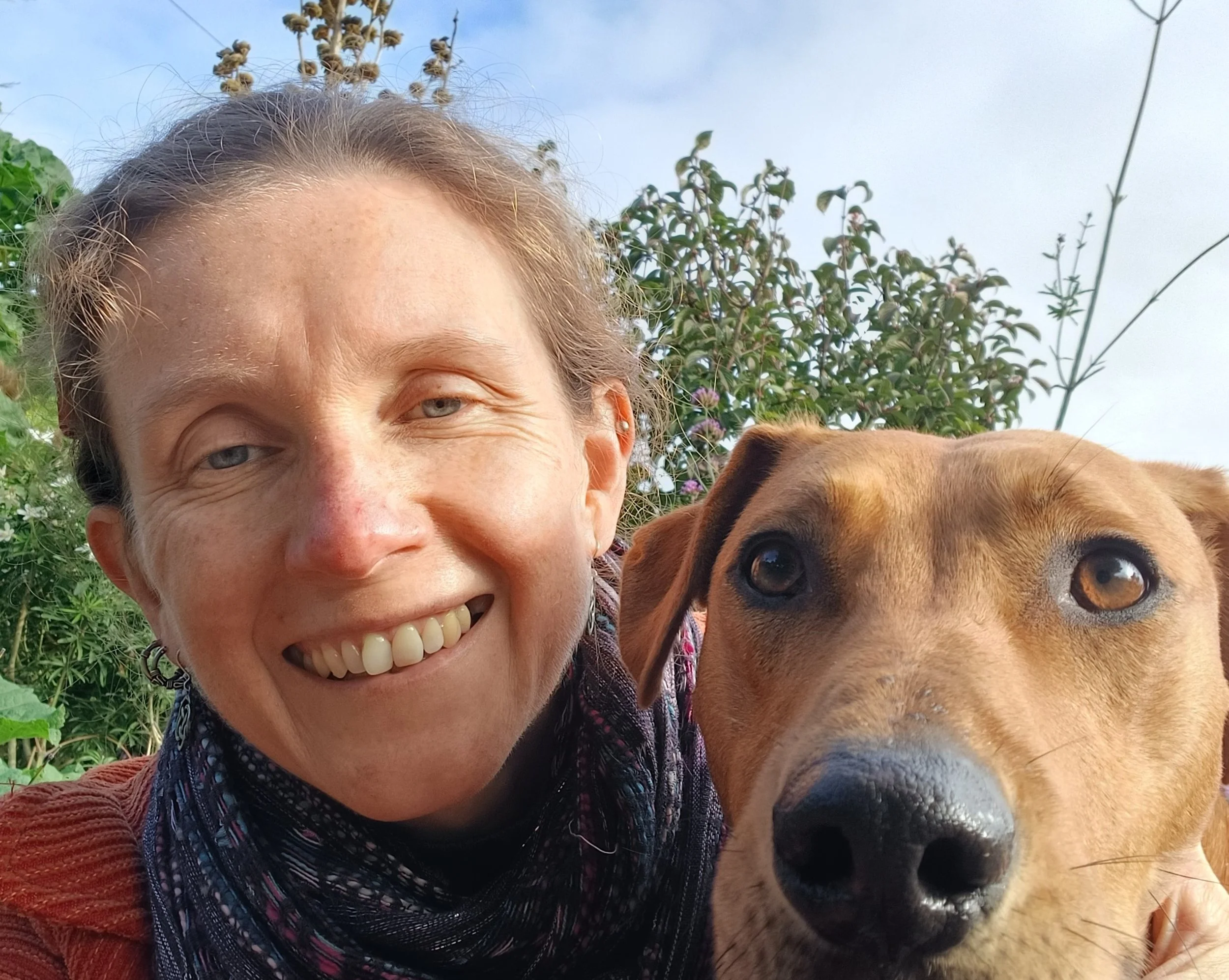 Photo of Rachel with dog with blue sky and bushes in the background.