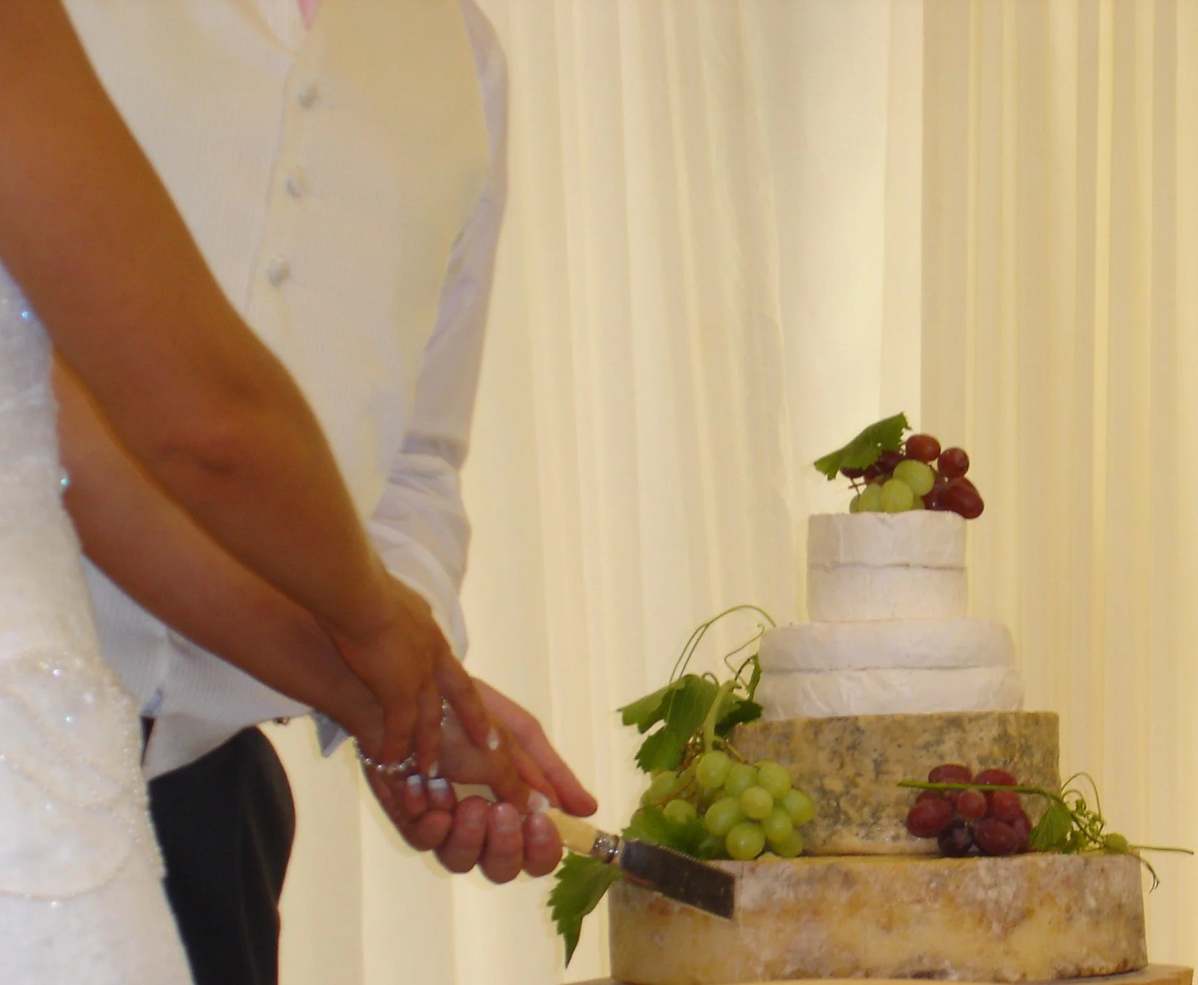 Couple cutting towering cake of cheese