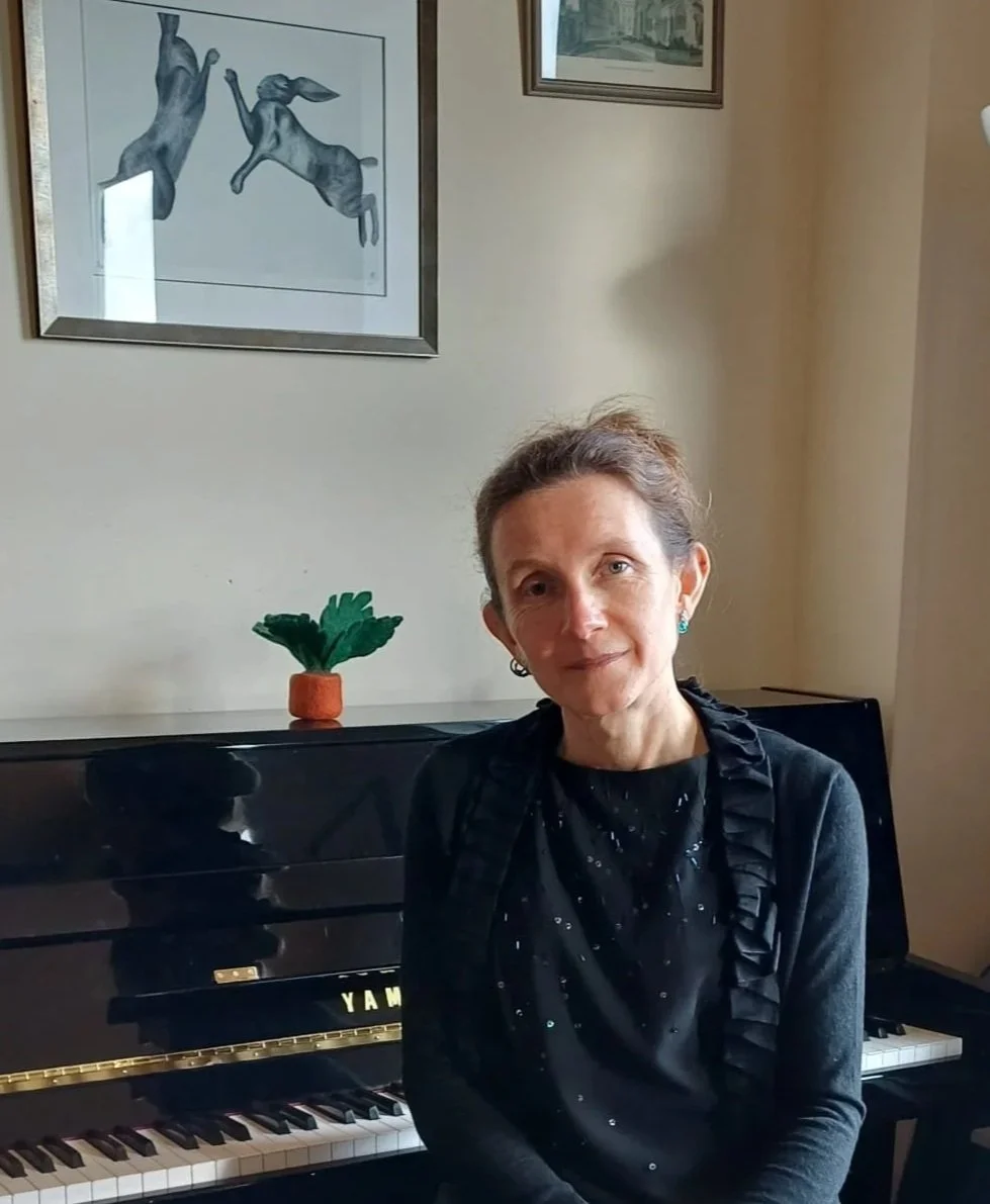 Rachel Peatfield, Celebrant, sitting by black piano