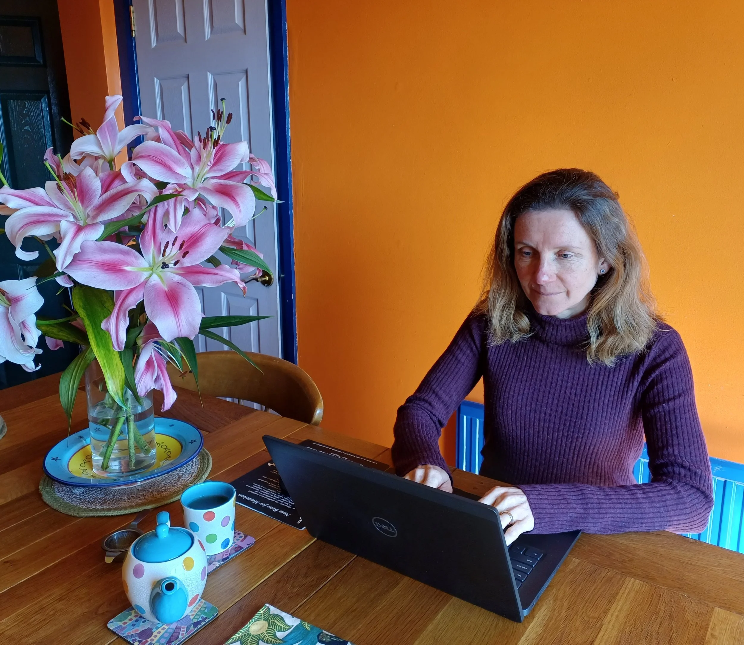 Rachel writing a ceremony on a laptop at a table with lilies in a vase